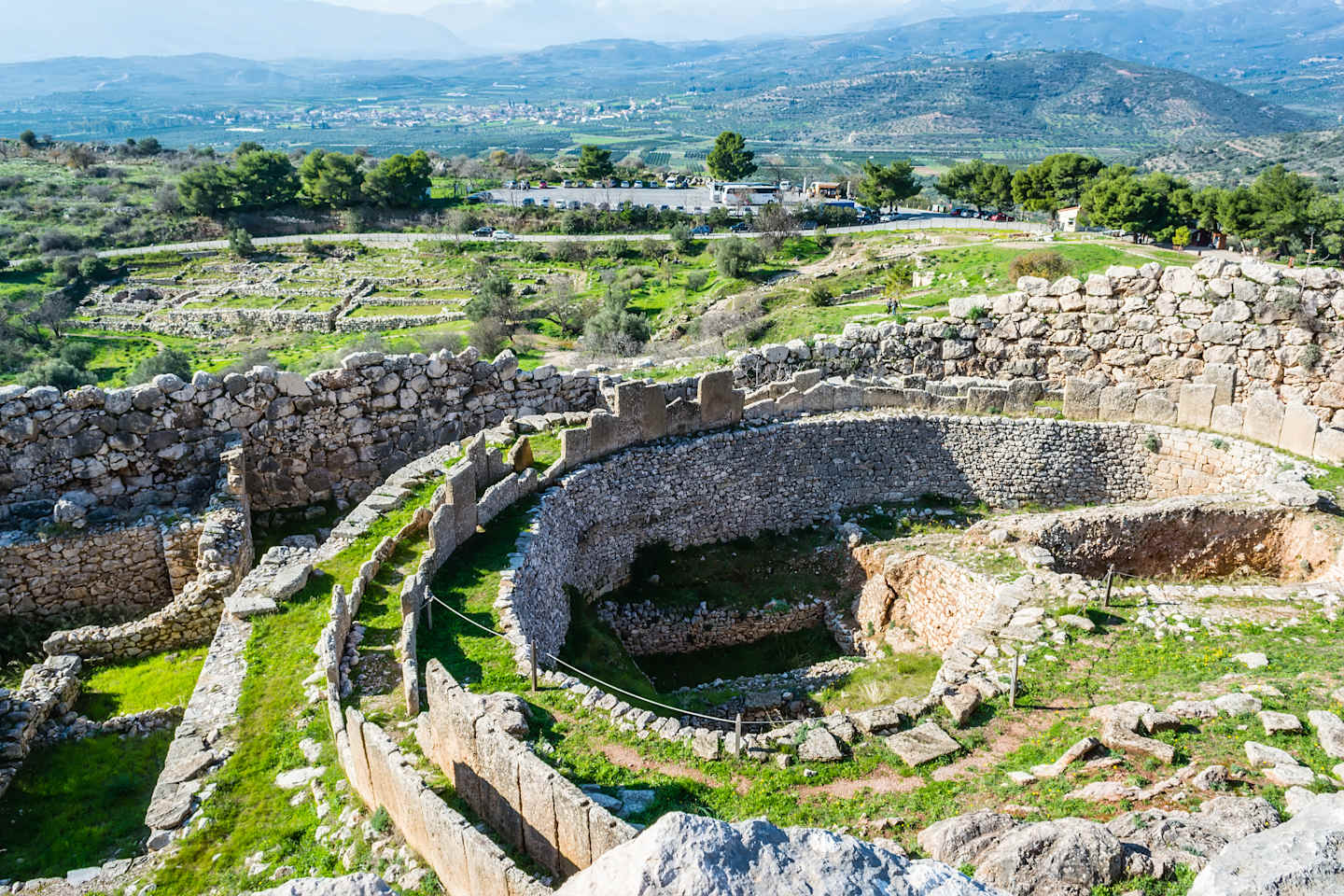 Sprawling ancient ruins nestled amidst lush greenery, with a mountainous backdrop in the distance.