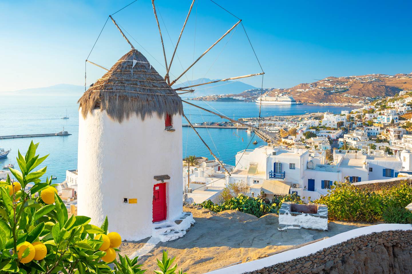 A picturesque windmill stands atop a hill, overlooking the vibrant, whitewashed buildings and the sparkling blue waters of the harbor below.