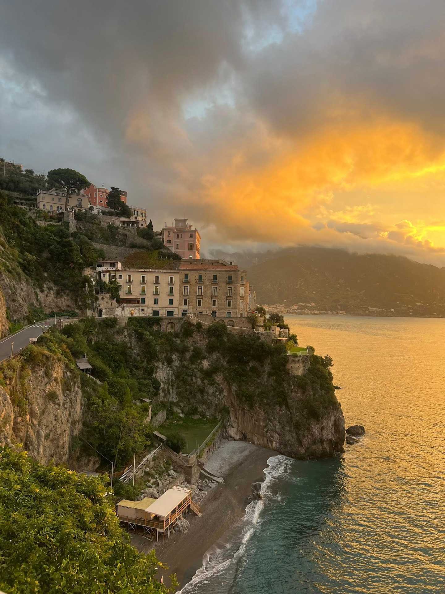 A picturesque coastal town nestled on a cliff, with colorful buildings and a dramatic sunset sky casting a warm glow over the tranquil waters below.