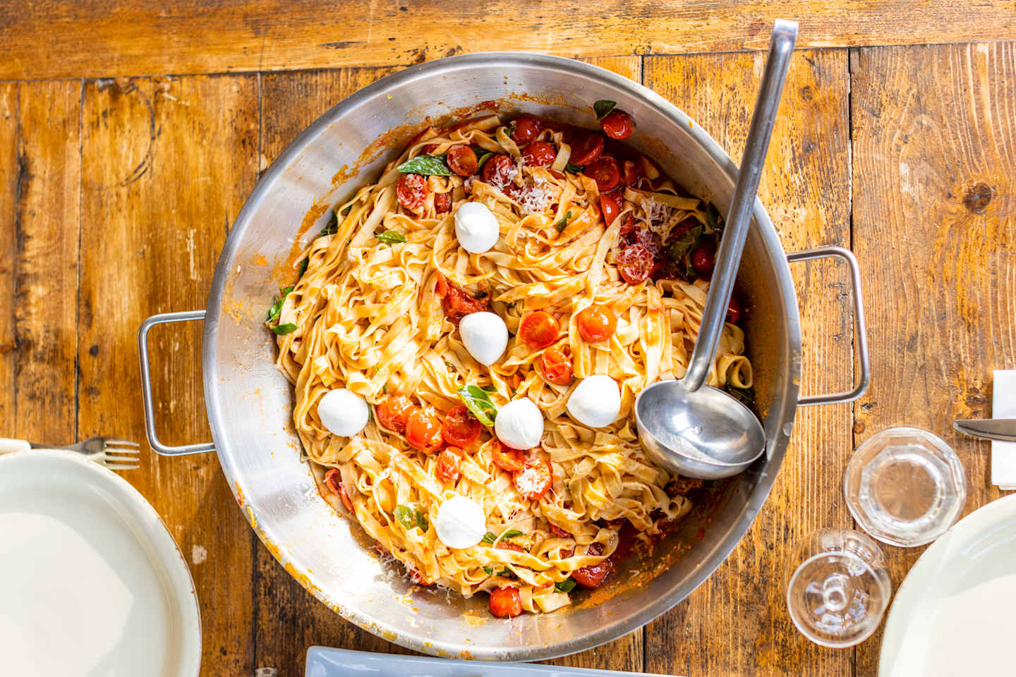 A large oval dish filled with a savory pasta dish, surrounded by various kitchen utensils and a wooden background.