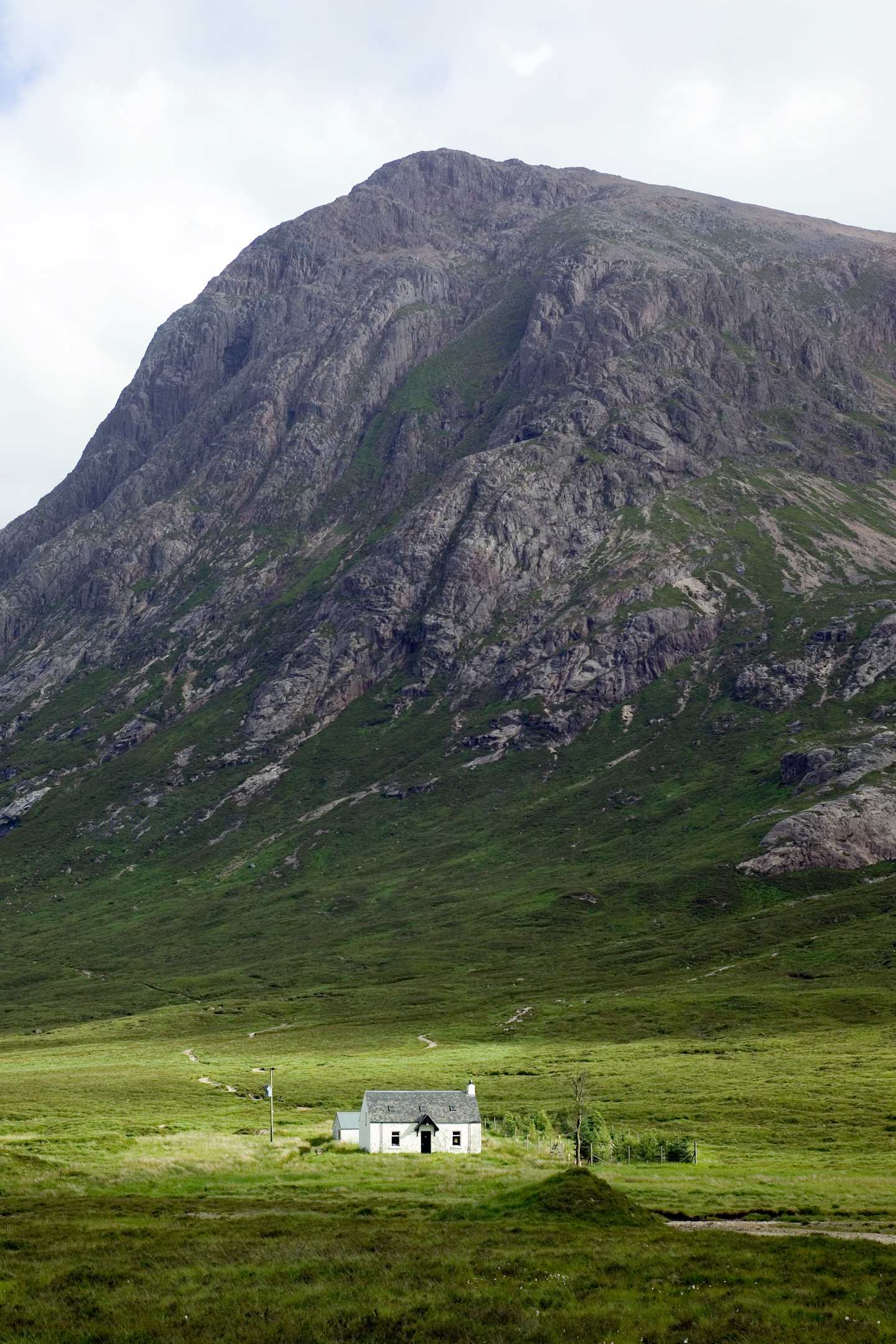 A rugged, mountainous landscape with a grassy foreground and a few small buildings nestled in the valley below.
