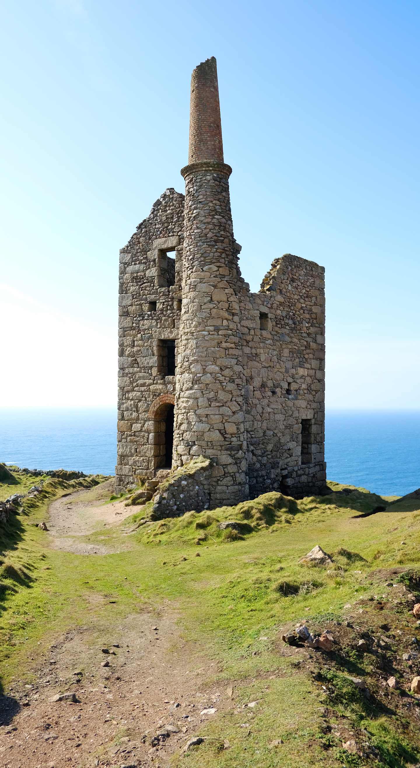 A ruined stone tower stands atop a grassy hill, overlooking the vast expanse of the ocean in the background.