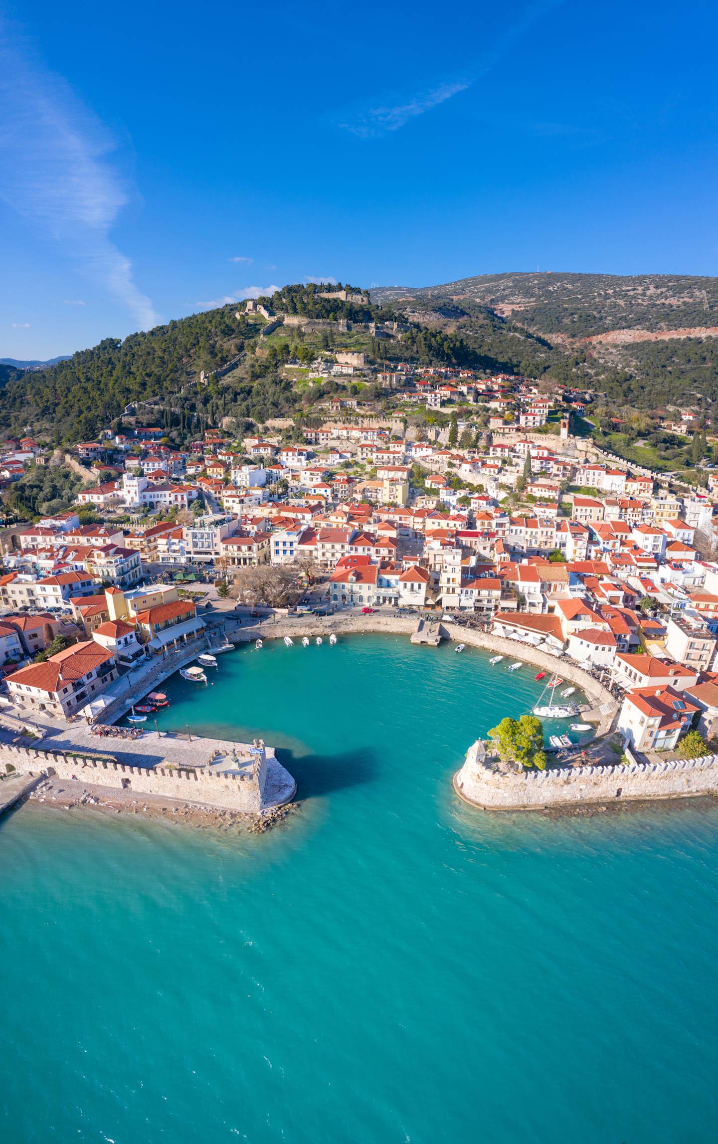 A picturesque coastal town nestled between hills, with a vibrant harbor and crystal-clear turquoise waters in the foreground.
