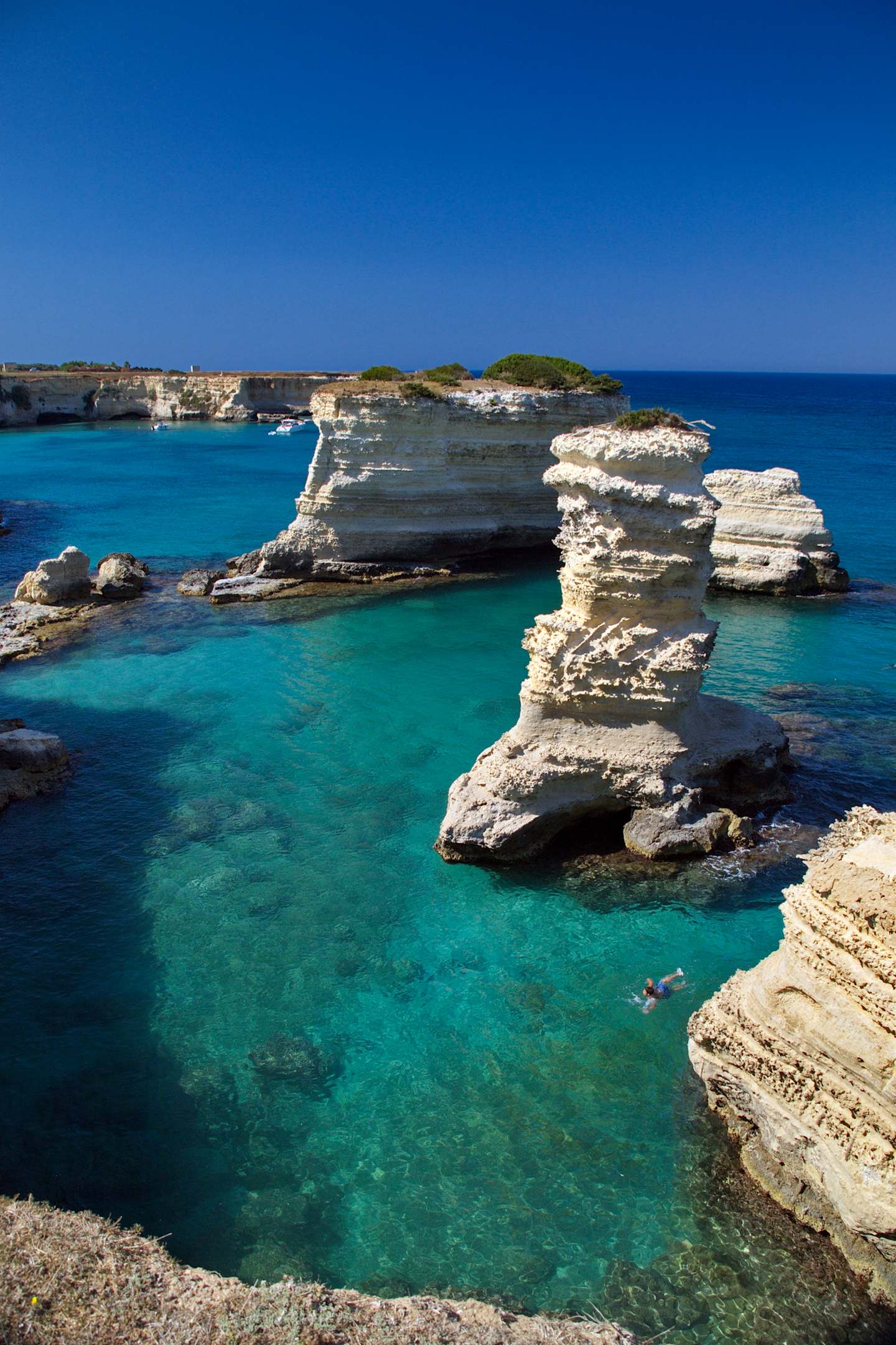 A stunning coastal landscape with rugged limestone cliffs, crystal-clear turquoise waters, and a picturesque village in the background.