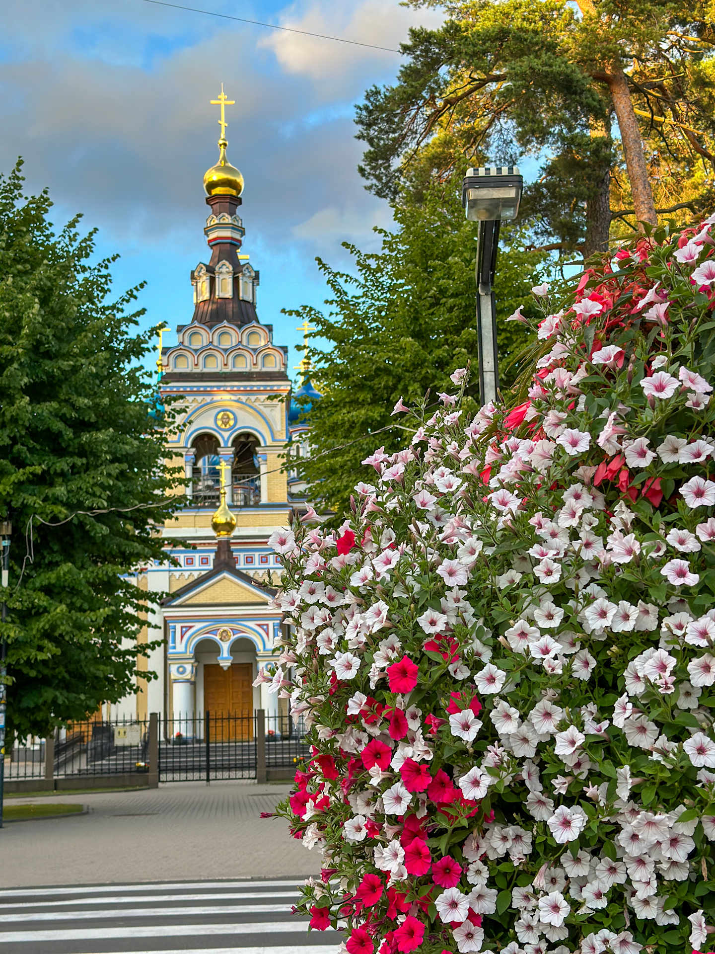 A colorful and vibrant scene featuring a Russian Orthodox church with a golden onion-shaped dome, surrounded by lush greenery and a profusion of blooming flowers in the foreground.