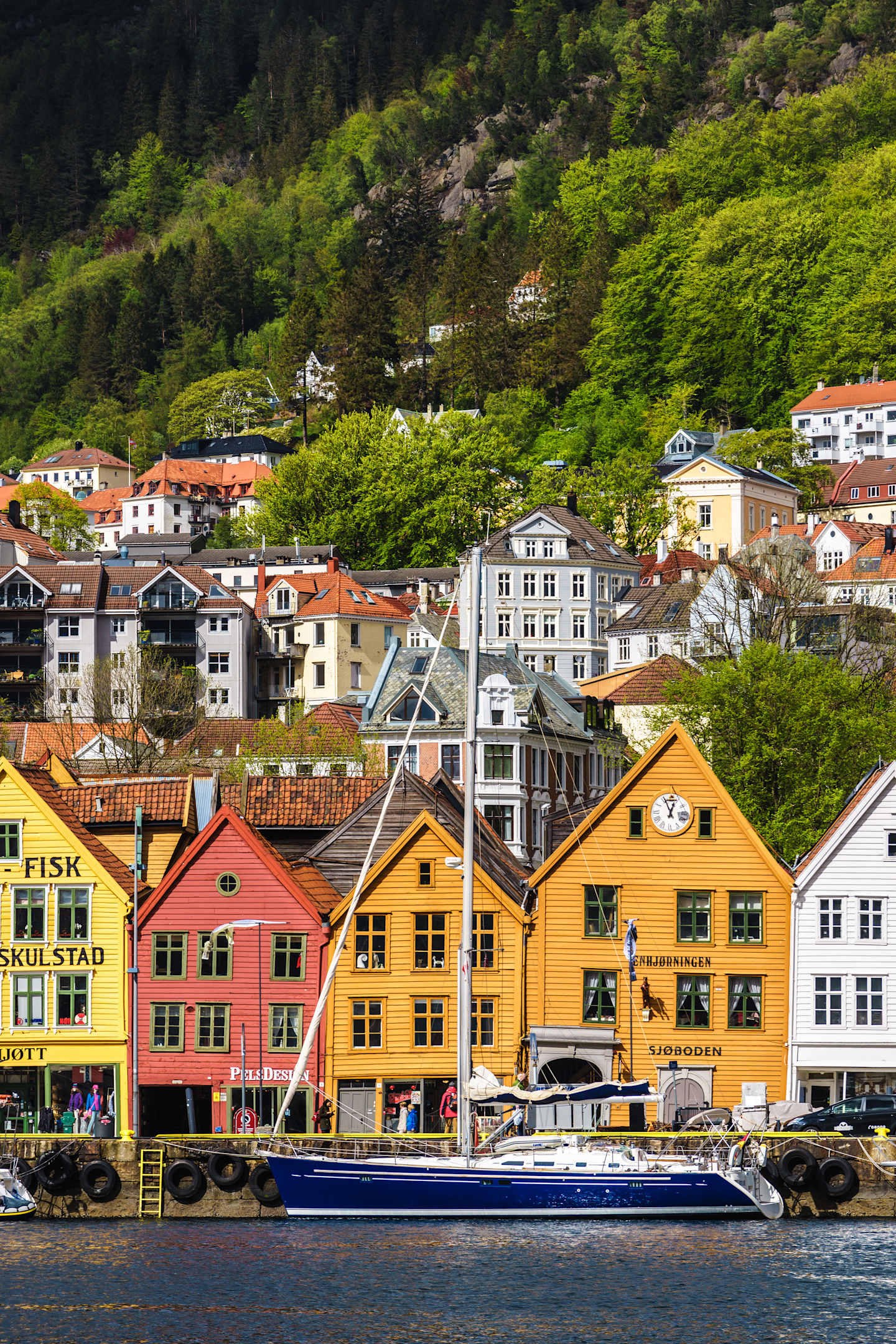 A colorful and picturesque town nestled in a lush, green landscape, with a harbor in the foreground featuring boats and ships.