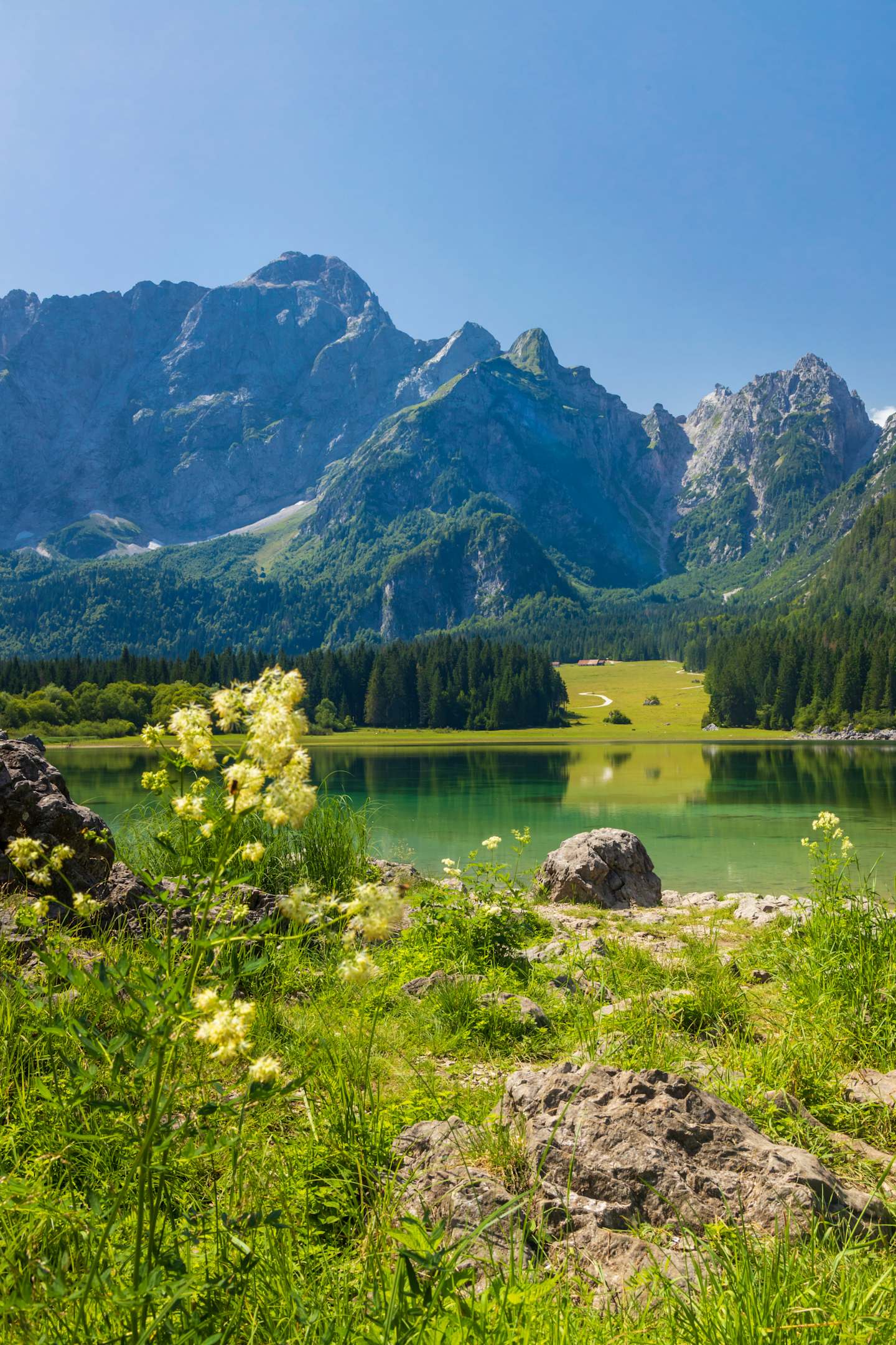 A serene mountain lake surrounded by lush green vegetation and towering peaks in the background, creating a picturesque natural landscape.
