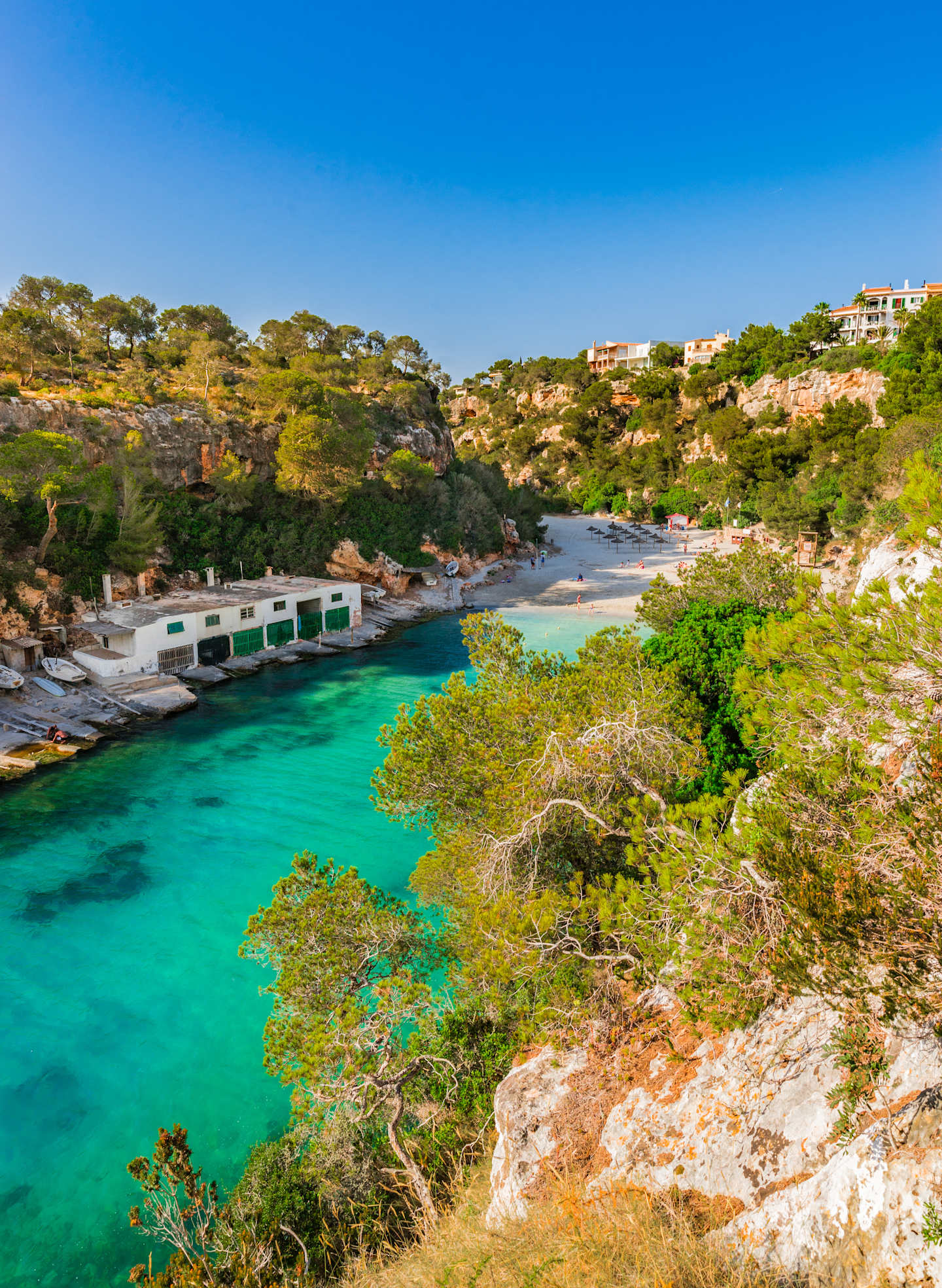 A picturesque cove with crystal-clear turquoise waters surrounded by lush, rocky cliffs and vegetation, with a small dock or pier visible in the foreground.