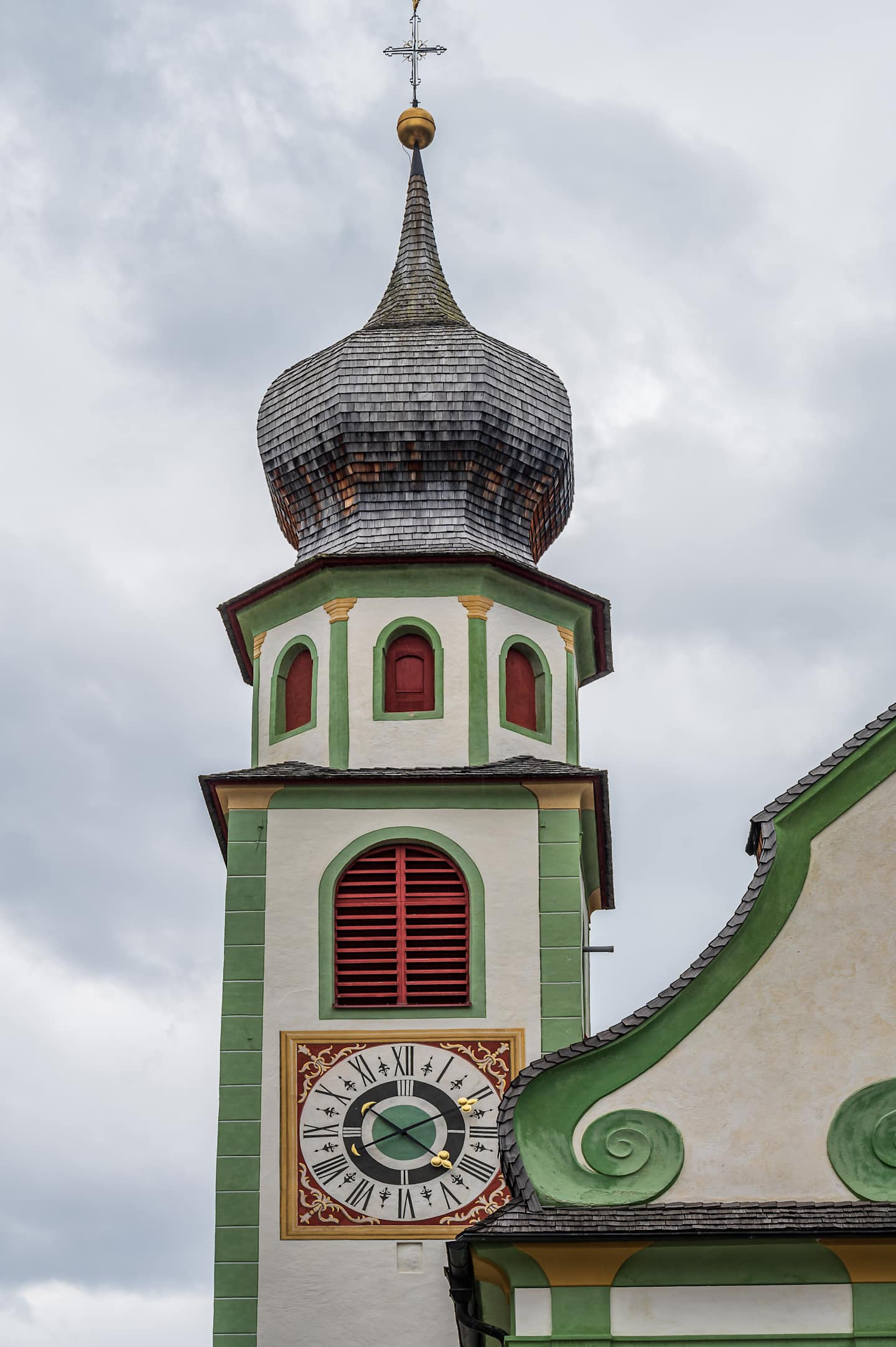 A colorful and ornate tower with a domed roof, featuring a clock face and intricate architectural details, set against a cloudy sky.