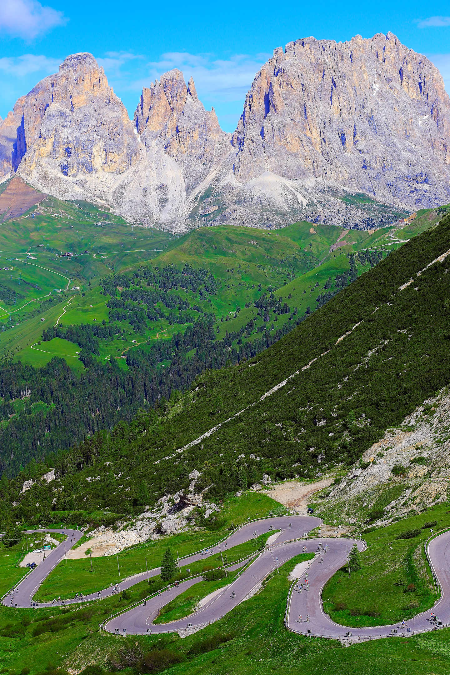Majestic snow-capped mountains rise in the background, while a winding road cuts through the lush, verdant landscape in the foreground.