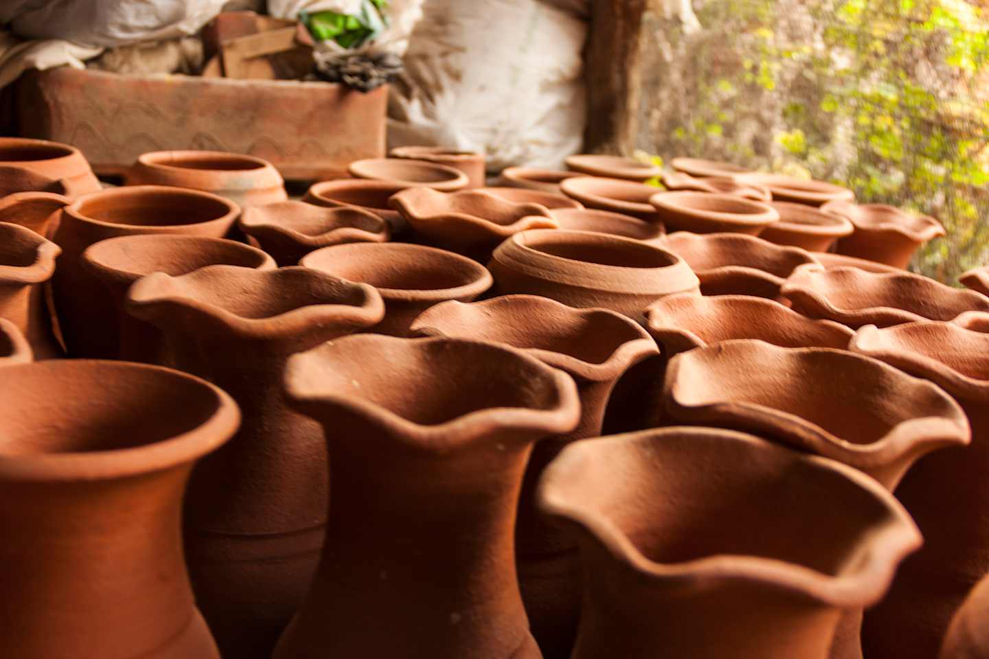 A collection of terracotta pots of various sizes and shapes, stacked and arranged in the foreground, with a blurred natural background visible.