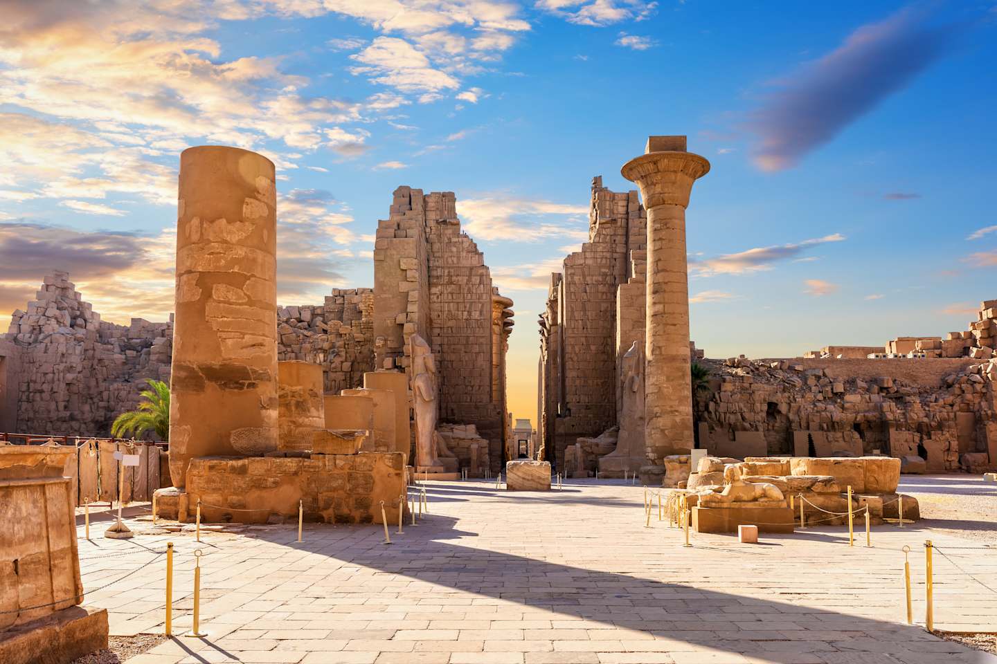 Towering ancient stone columns and ruins stand against a vibrant sky with clouds at sunset, creating a captivating and awe-inspiring scene.