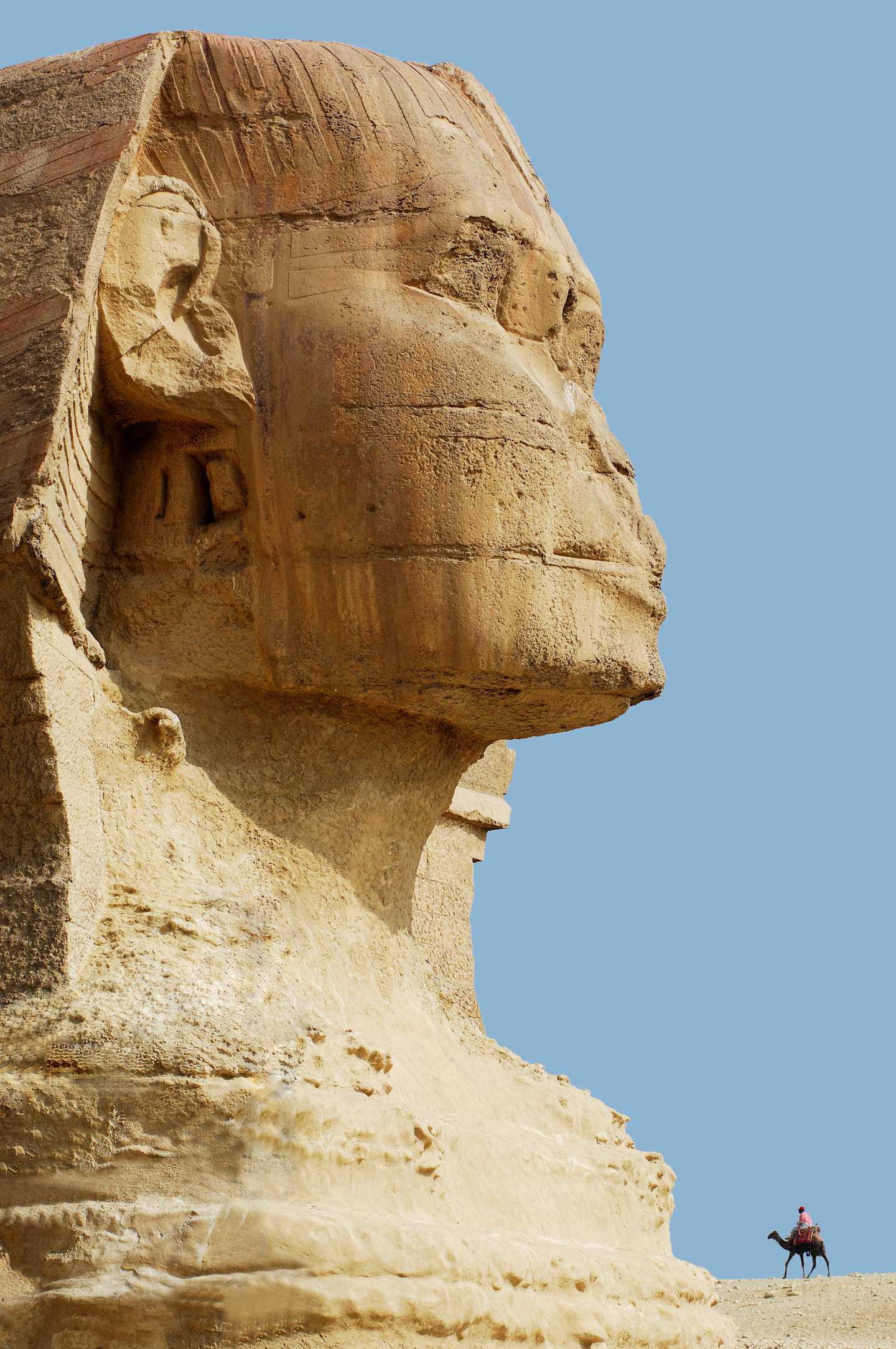 A massive ancient sphinx-like structure dominates the image, with a person riding a camel in the foreground against a clear blue sky.