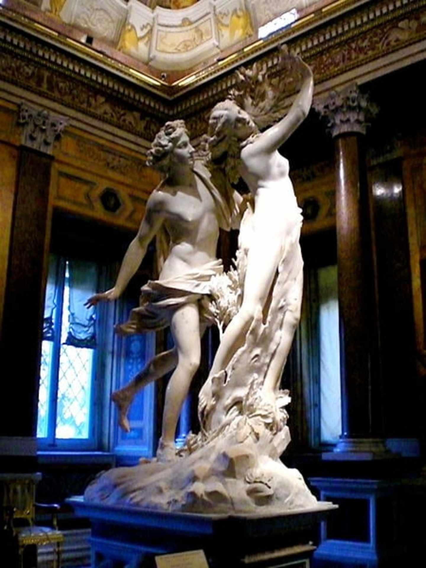 A grand, ornate interior with a large, dramatic marble sculpture depicting two figures in a dynamic, intertwined pose, set against a backdrop of intricate architectural details and decorative elements.