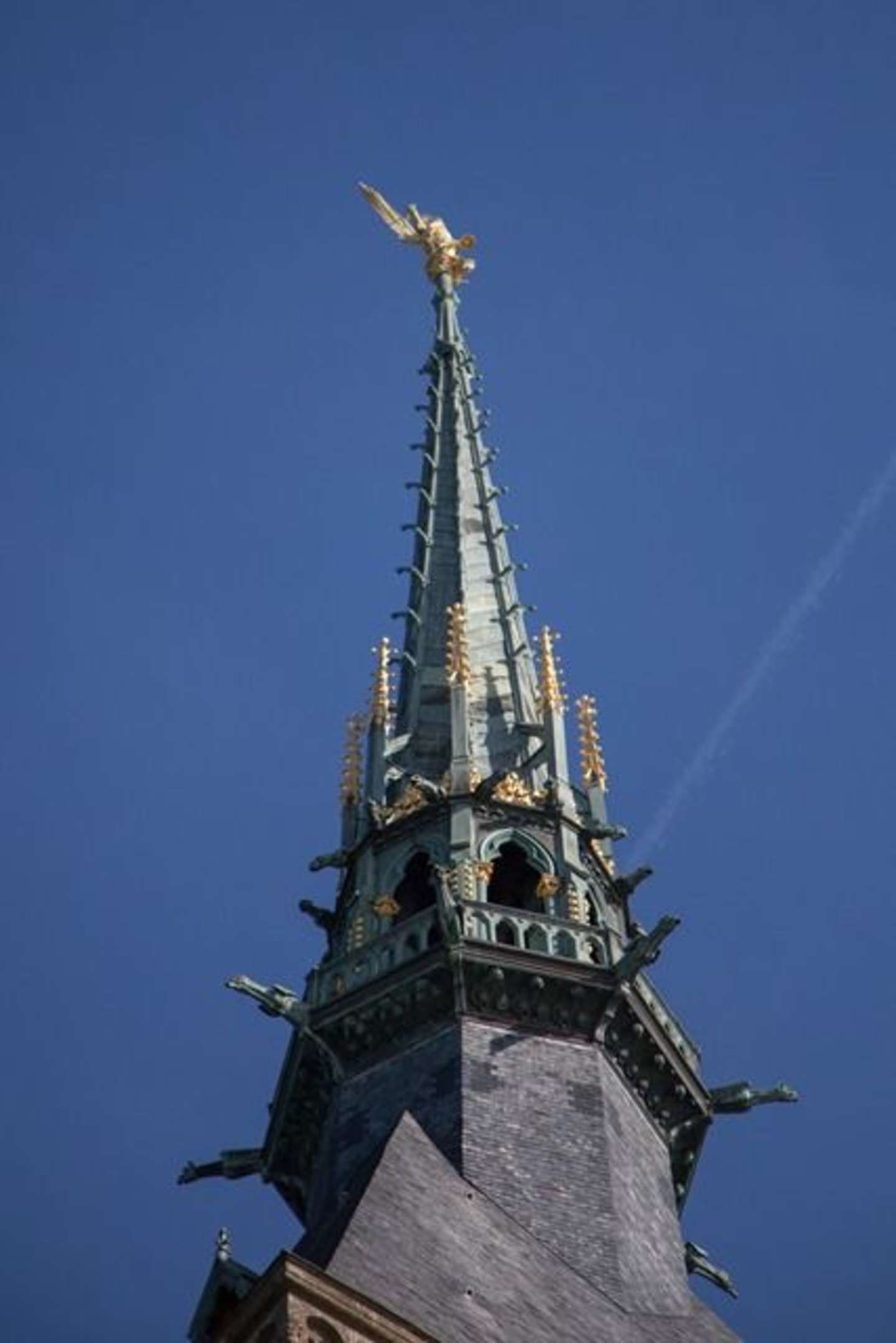 A tall, ornate spire with intricate architectural details stands against a clear blue sky.