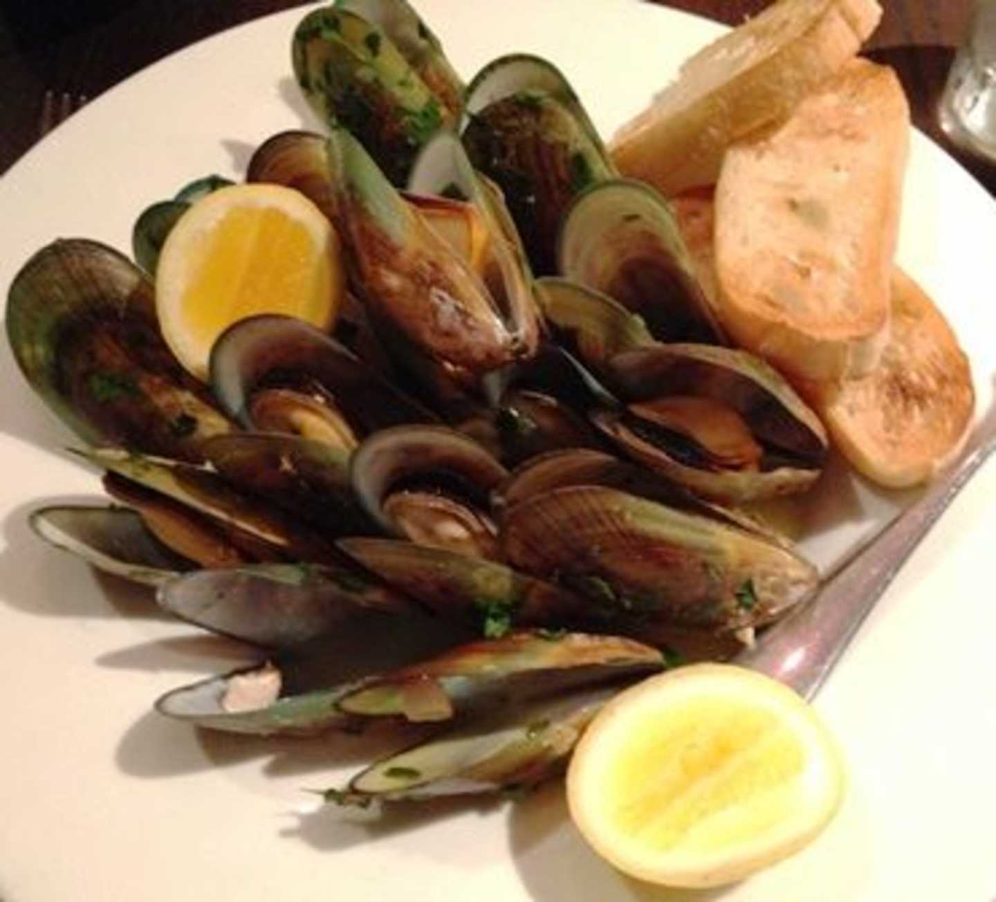 A plate filled with a variety of cooked mussels, accompanied by slices of lemon and a piece of bread on the side.
