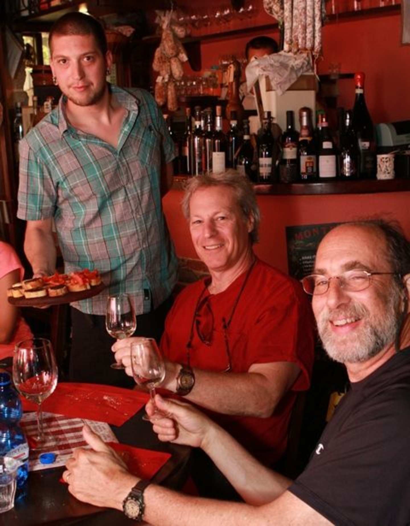 The image shows three men sitting at a table in what appears to be a bar or restaurant, enjoying drinks and conversation.
