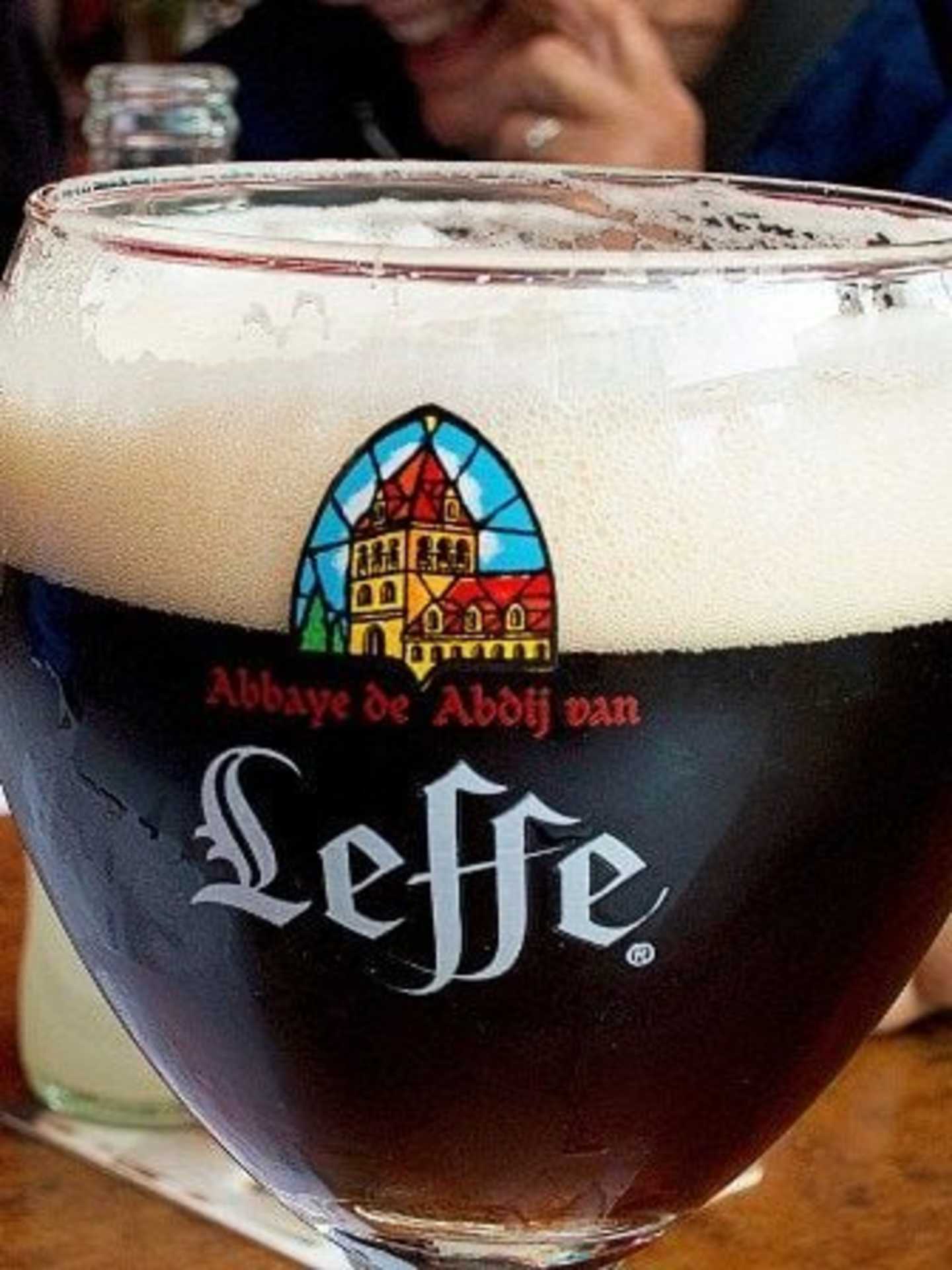 A glass of Leffe beer with the Leffe logo and a stained glass-style image of a church or abbey in the background.