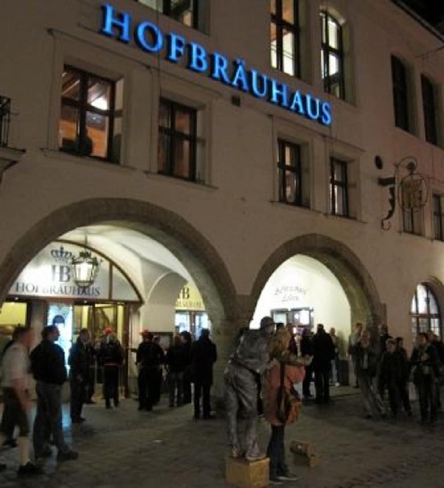 The image shows the exterior of a building called "Hofbrauhaus", with a crowd of people gathered outside the entrance.