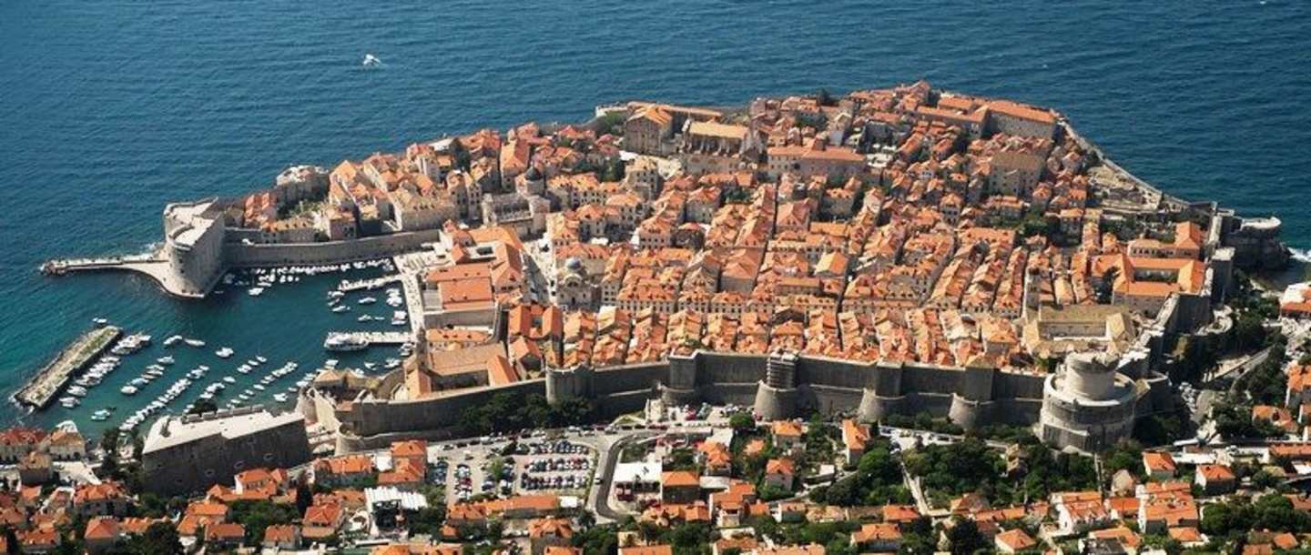 A densely packed coastal town with red-tiled roofs and narrow streets, surrounded by a deep blue sea.