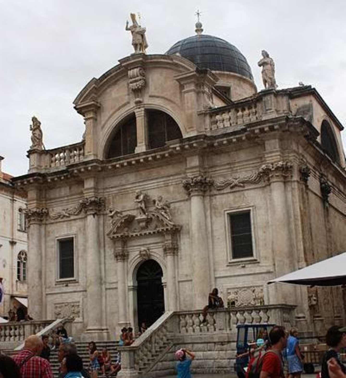 A grand, ornate building with a domed roof and intricate architectural details, surrounded by people in the foreground.
