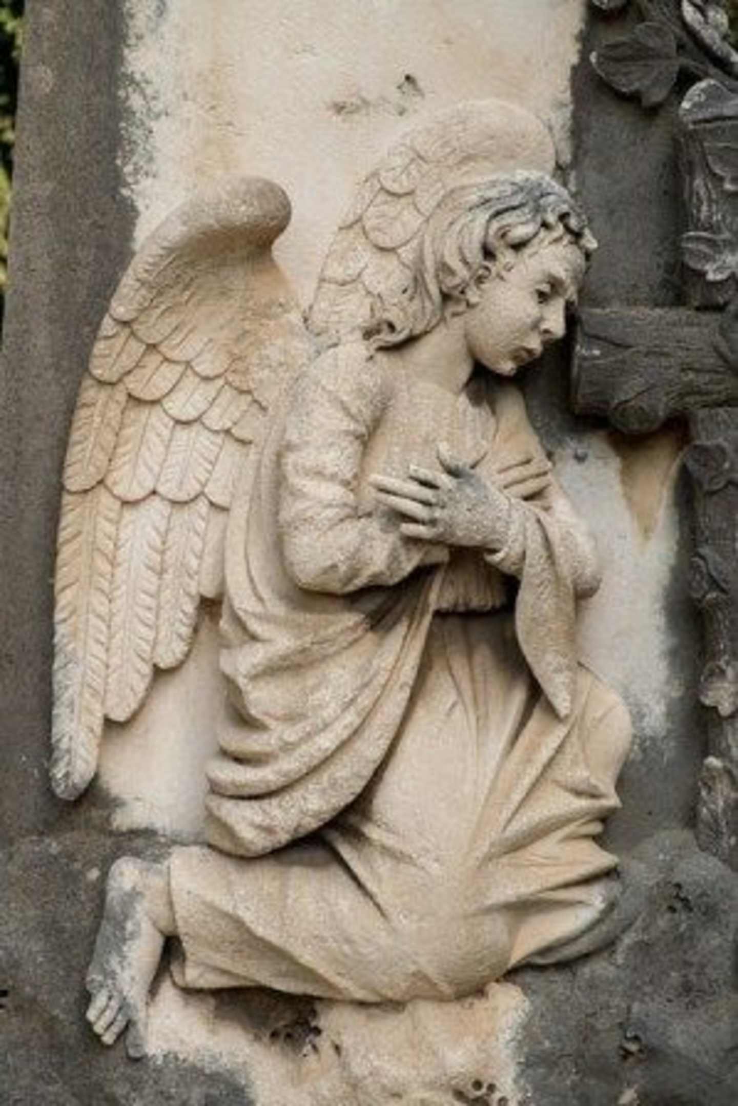 A stone sculpture of an angel with wings, sitting in a contemplative pose, against a backdrop of weathered stone structures.