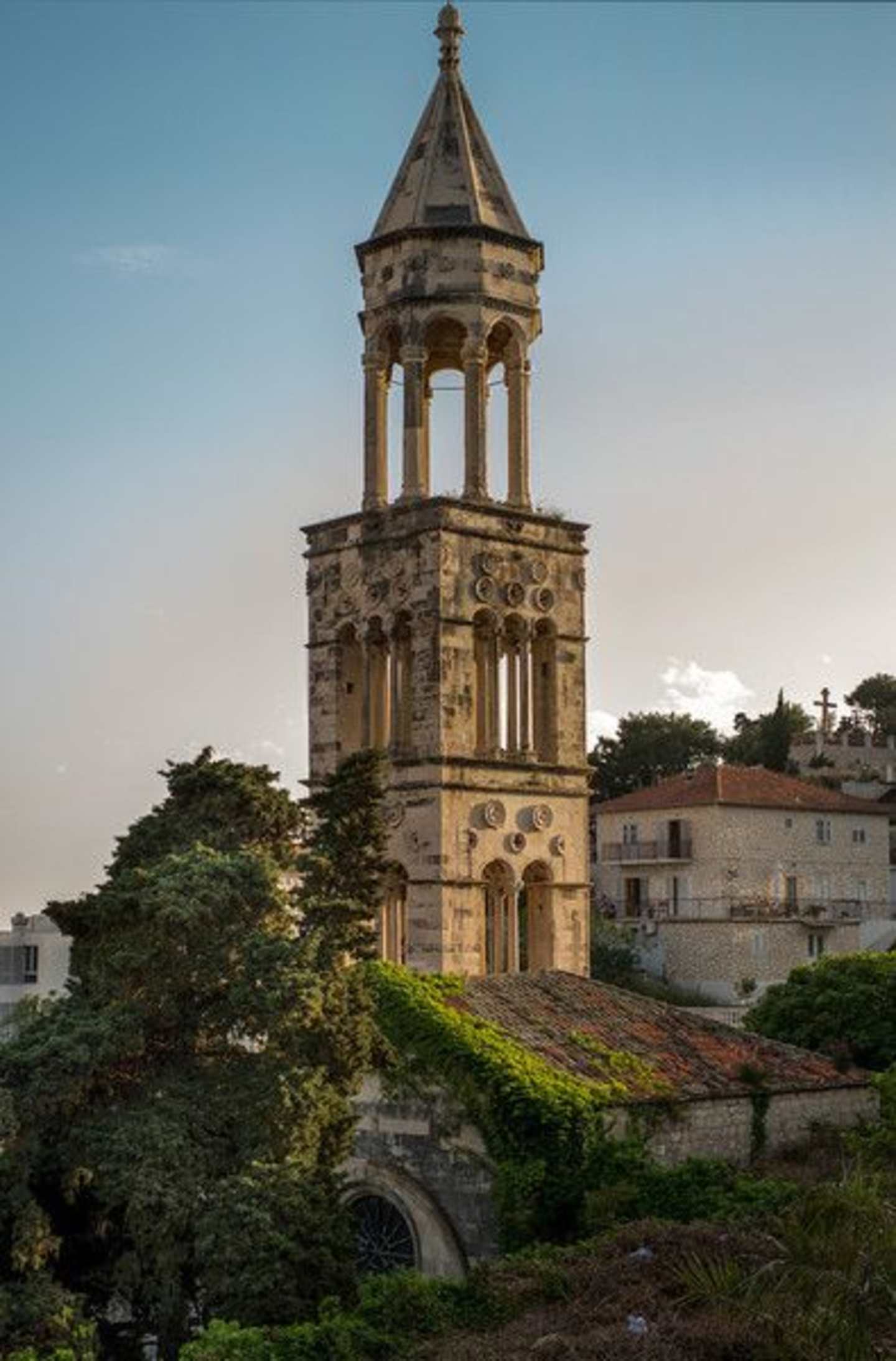 A stone tower with a domed roof stands prominently in the foreground, surrounded by lush greenery and buildings in the background.