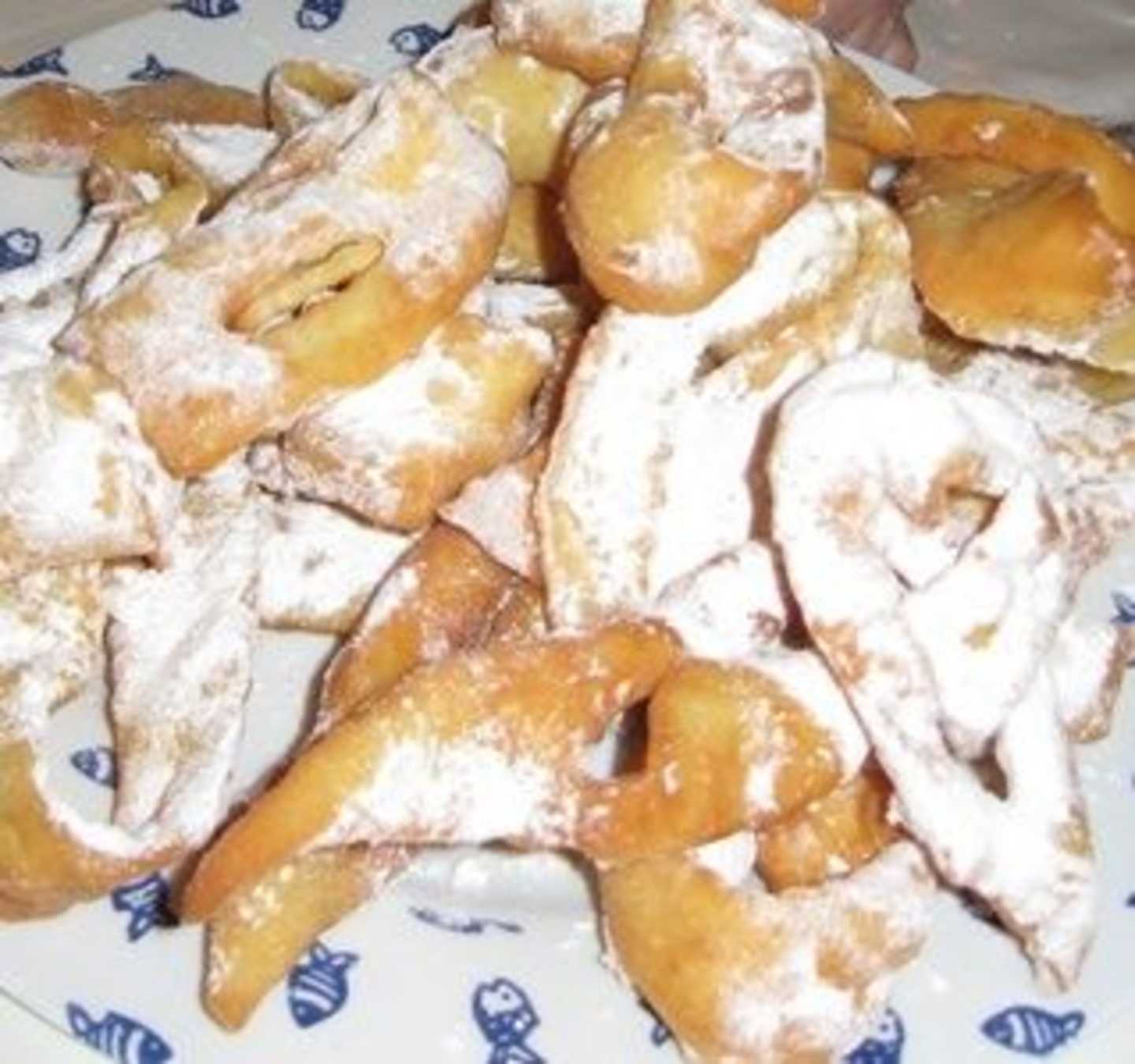 A plate filled with various fried pastries, some dusted with powdered sugar, resting on a patterned background.
