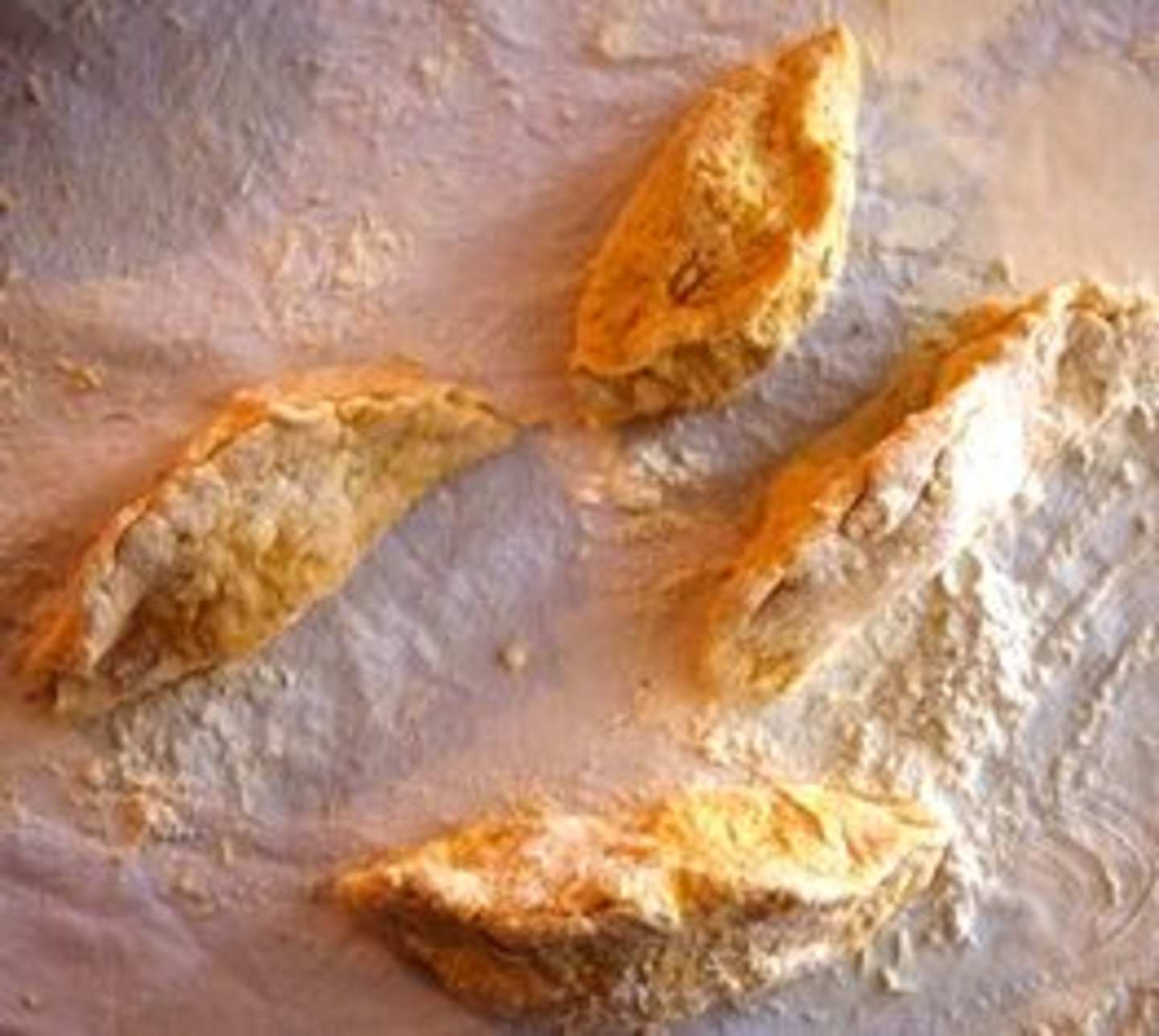 Freshly baked bread slices with a golden-brown crust lie on a lightly dusted surface, creating a warm and inviting scene.