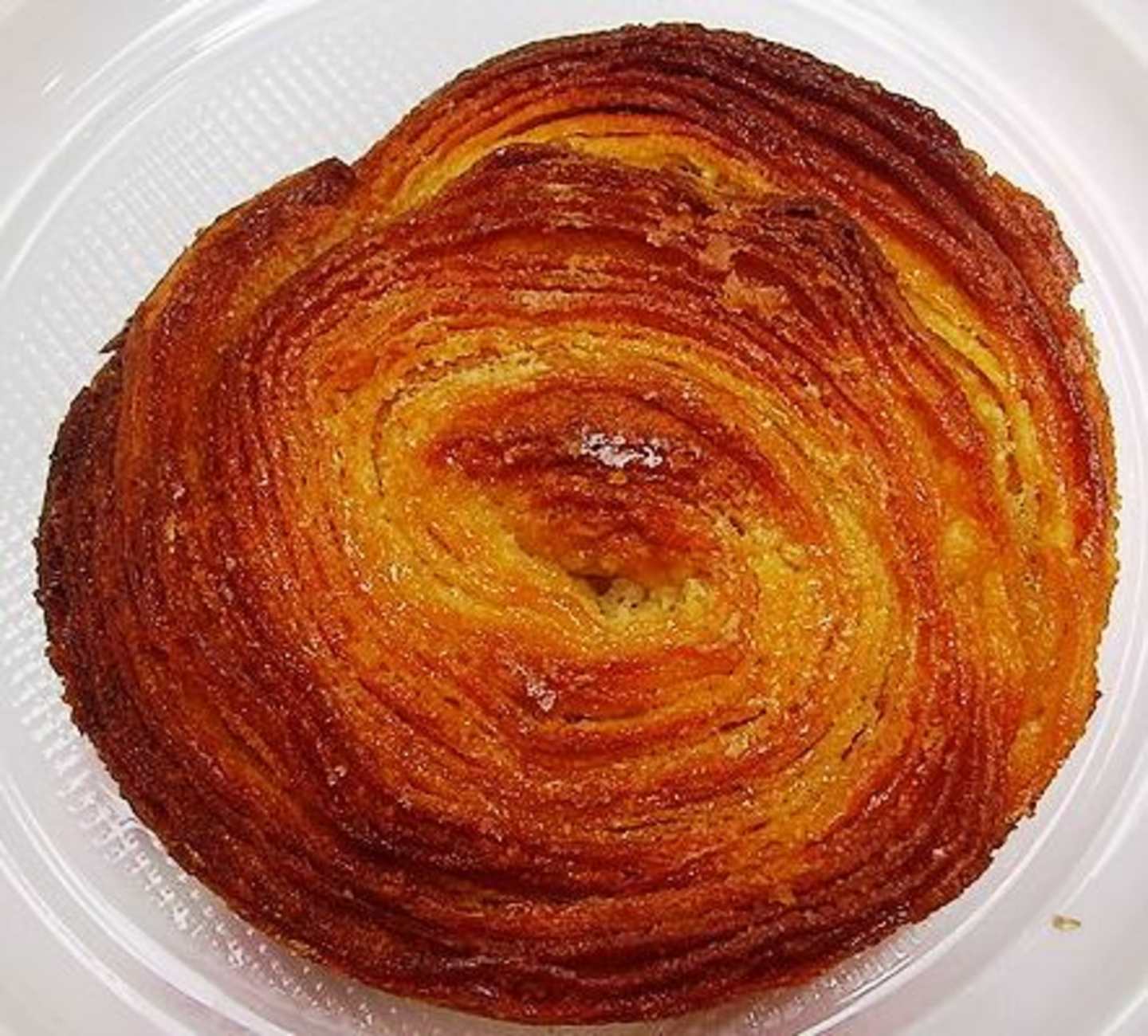 A beautifully baked pastry with a swirling pattern of golden-brown layers, resting on a white plate.