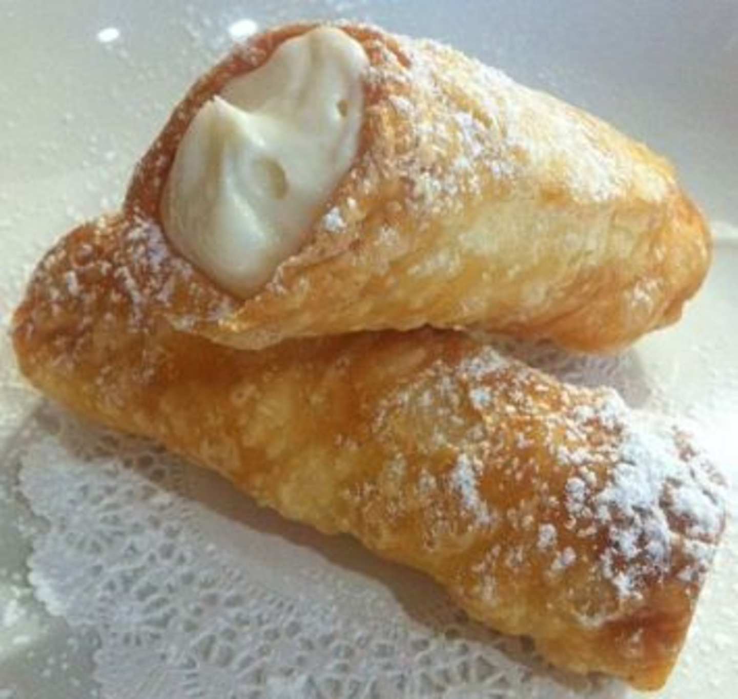 A golden, flaky pastry filled with a creamy, white substance, dusted with powdered sugar, sits on a reflective surface.