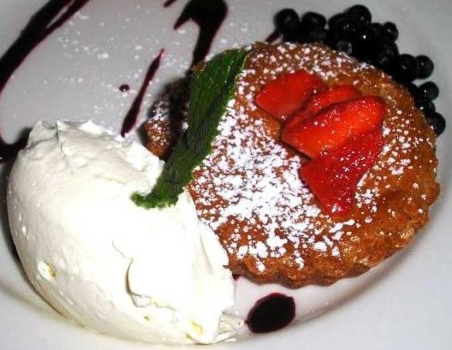 A delectable dessert featuring a golden-brown pastry shell filled with vibrant red strawberries, accompanied by a scoop of creamy white ice cream and garnished with fresh mint leaves and dark berries.
