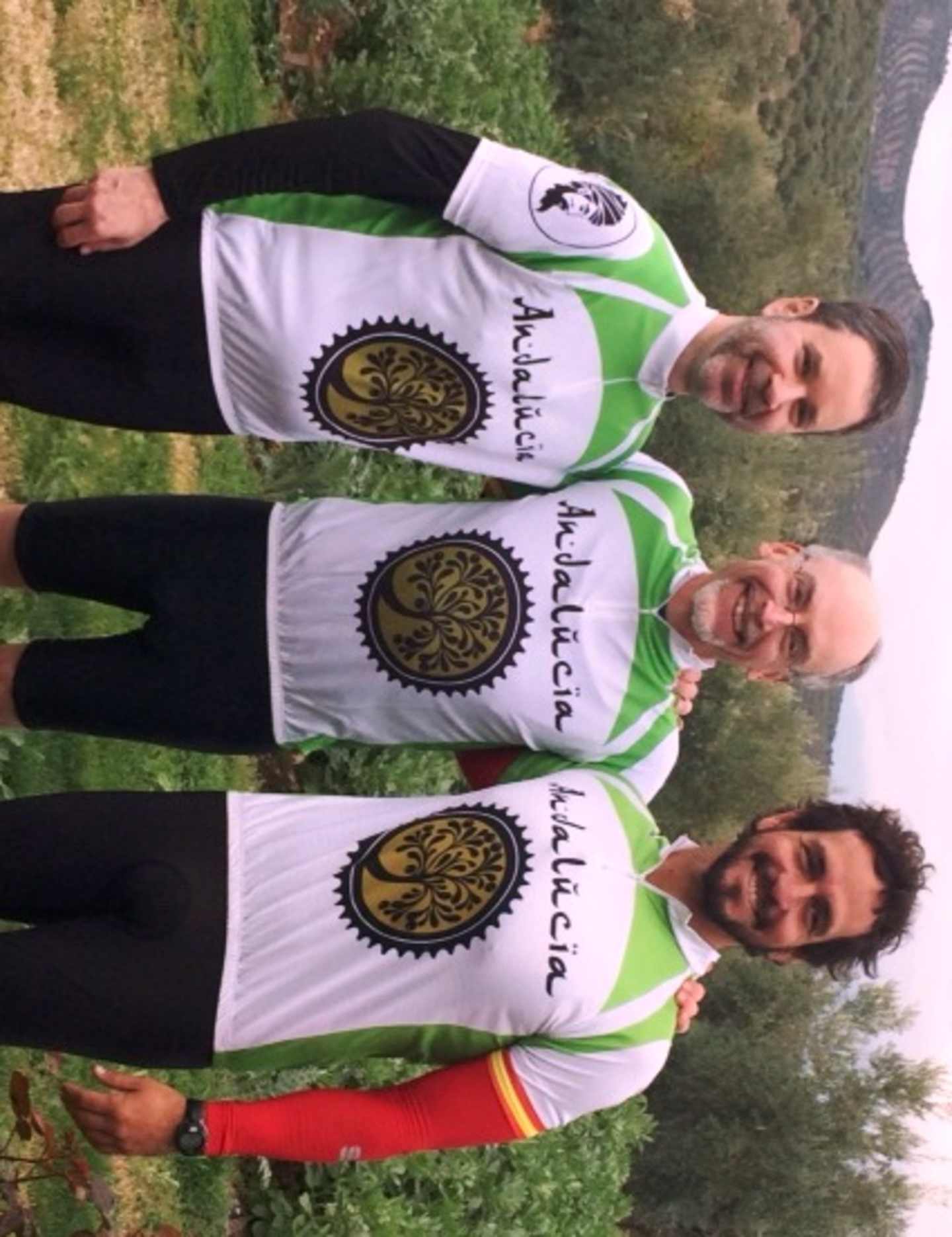 Three individuals wearing matching green and white jerseys with a logo on the front, standing in a grassy outdoor setting.