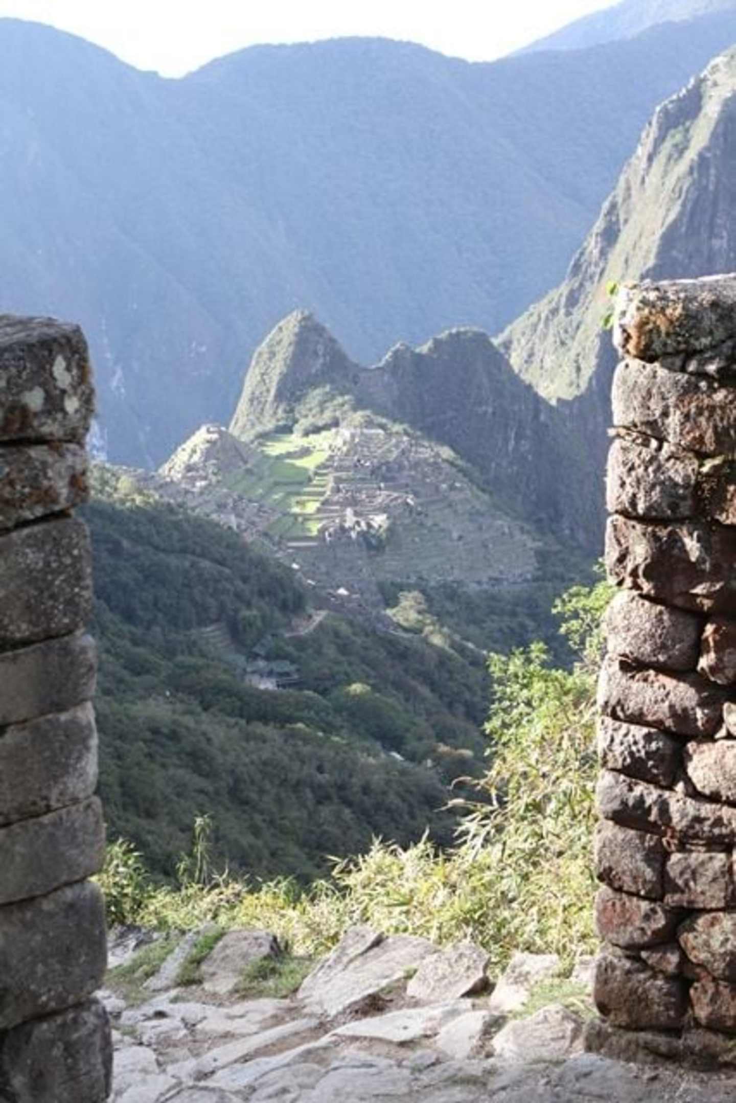 A rugged, mountainous landscape with a winding path leading through the foreground, surrounded by towering peaks and lush greenery in the background.