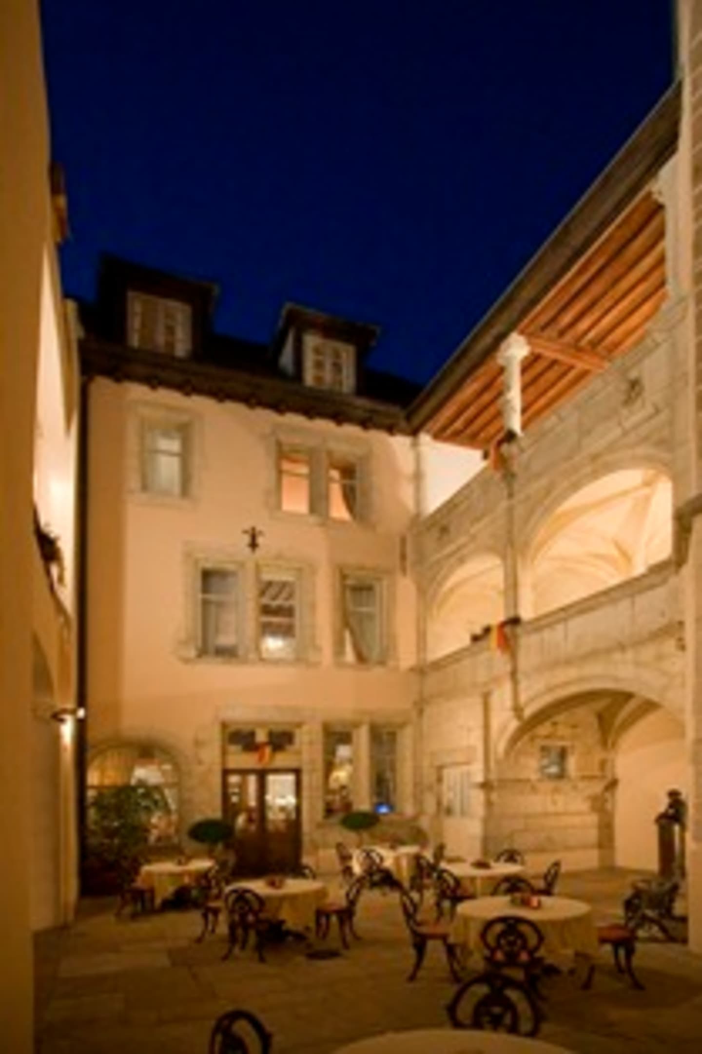 A cozy courtyard with ornate architectural features, illuminated by warm lighting at night, with various outdoor furniture and decor elements.