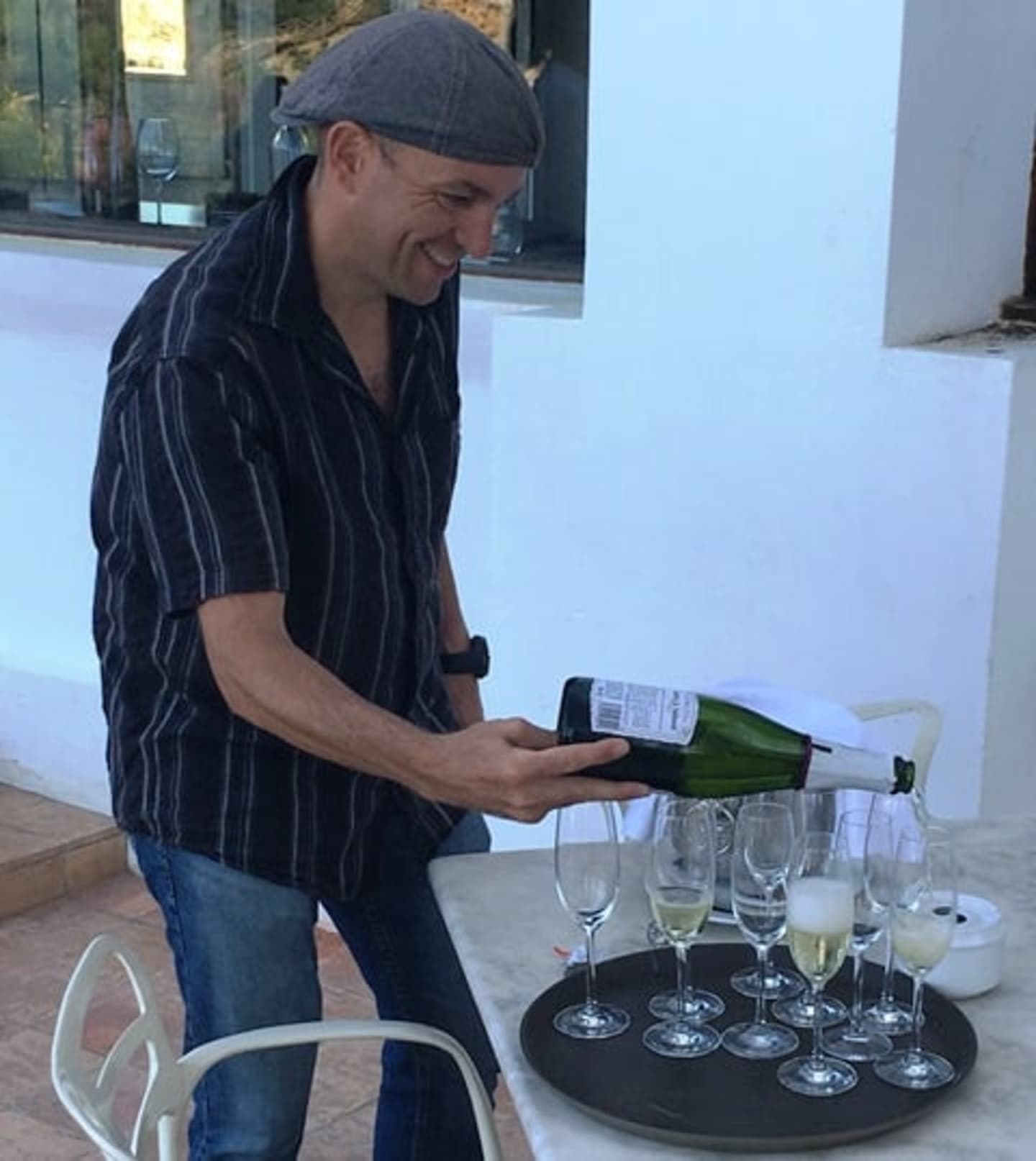 A man in a striped shirt is pouring wine into glasses on a tray in what appears to be a restaurant or bar setting.