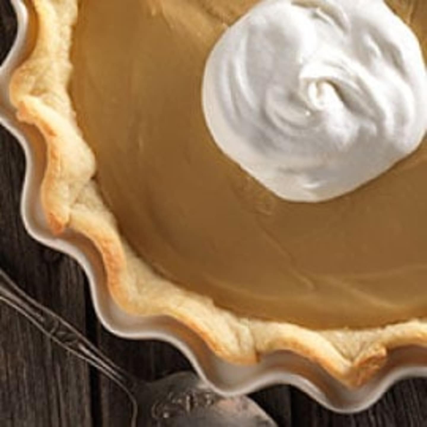 A flaky pie crust with a dollop of whipped cream sits on a dark wooden surface.