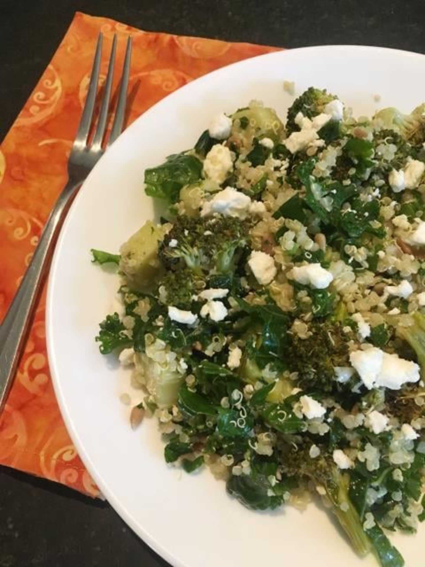 A white plate filled with a colorful salad of greens, vegetables, and crumbled cheese, set on an orange patterned cloth with a fork in the foreground.