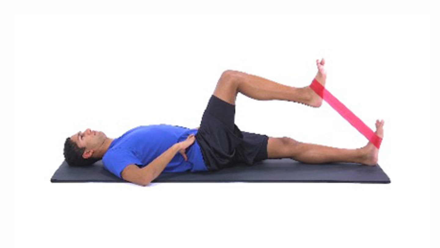 A person in a blue shirt is lying on a yoga mat, performing a stretching exercise with a resistance band.