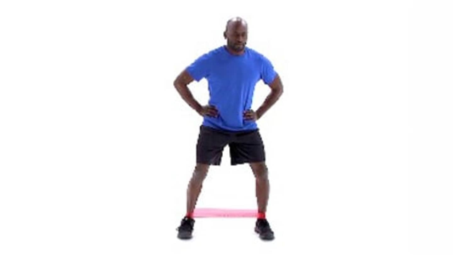 A person wearing a blue shirt and black shorts stands on a pink exercise mat against a white background.