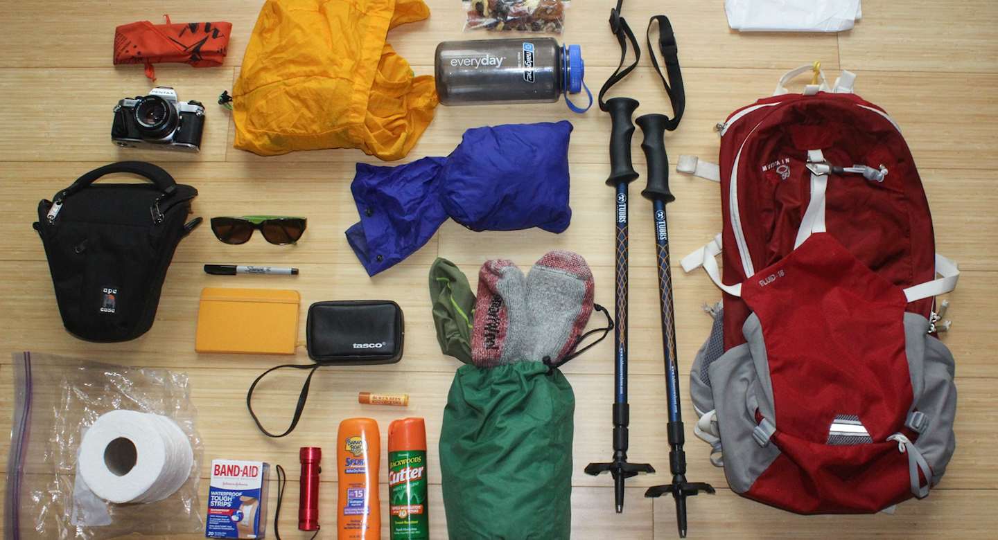 An assortment of outdoor gear, including backpacks, clothing, and hiking equipment, is displayed on a wooden surface.