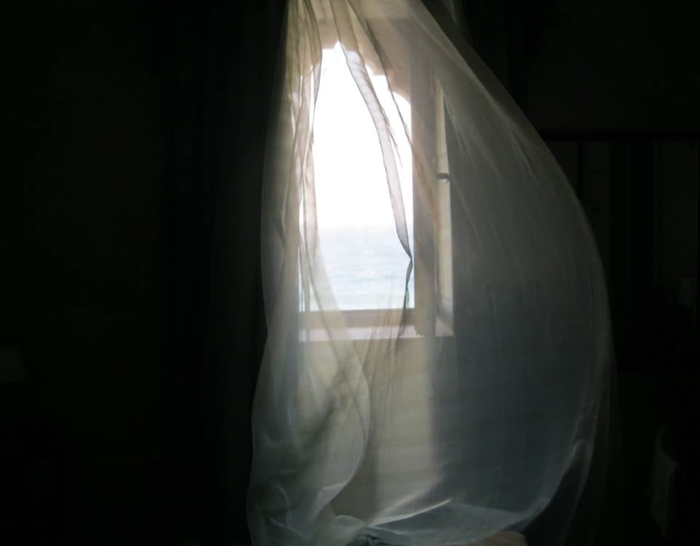 Sheer white curtains billow in the soft light, revealing a glimpse of the distant landscape beyond the window.