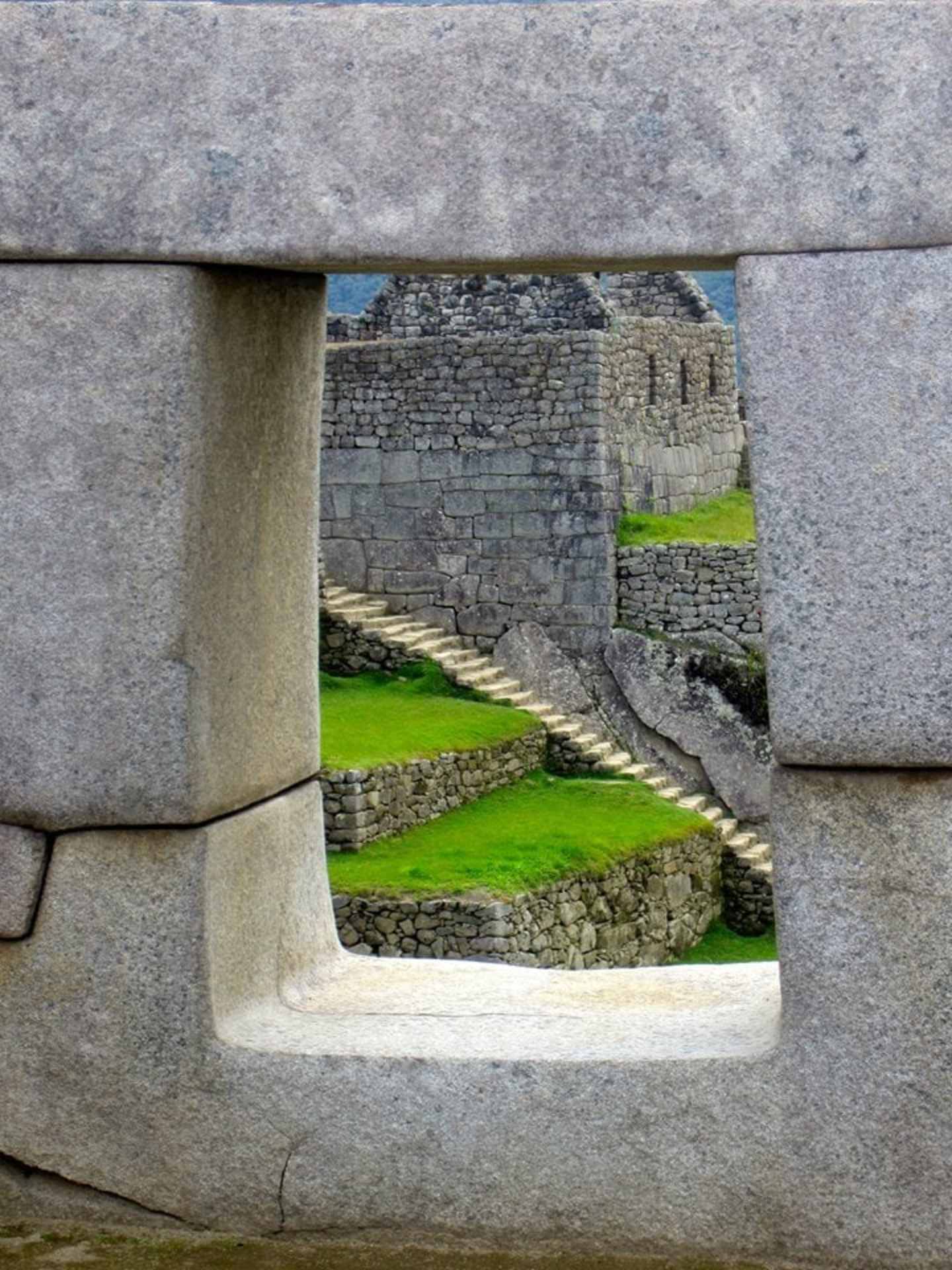 A stone archway frames a view of a grassy, terraced landscape with ancient stone structures in the background.