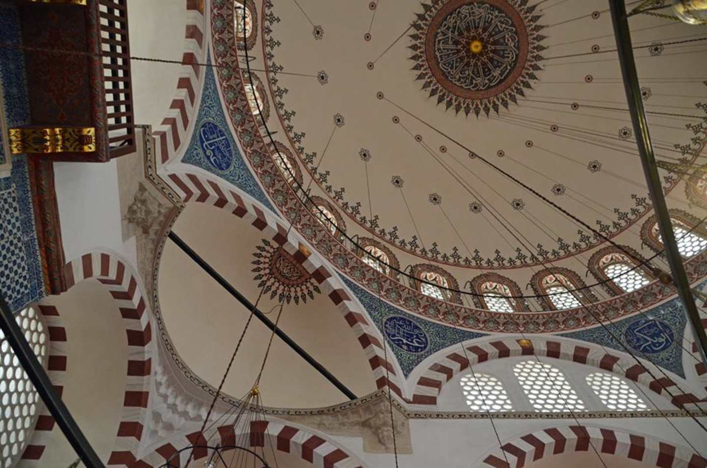 A grand, ornately decorated domed ceiling with intricate patterns, geometric designs, and colorful tiles adorns the interior of what appears to be a religious or cultural structure.