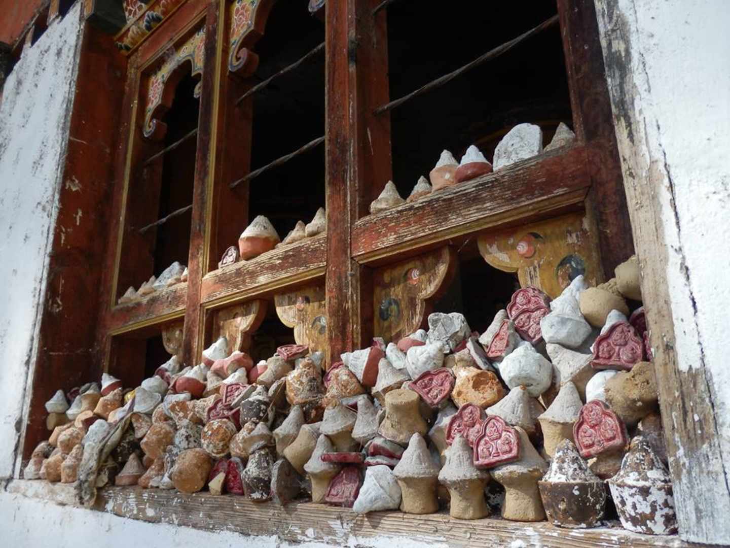 A wooden window frame filled with various ceramic figurines, some of which appear to be damaged or worn, set against a backdrop of a dilapidated interior.