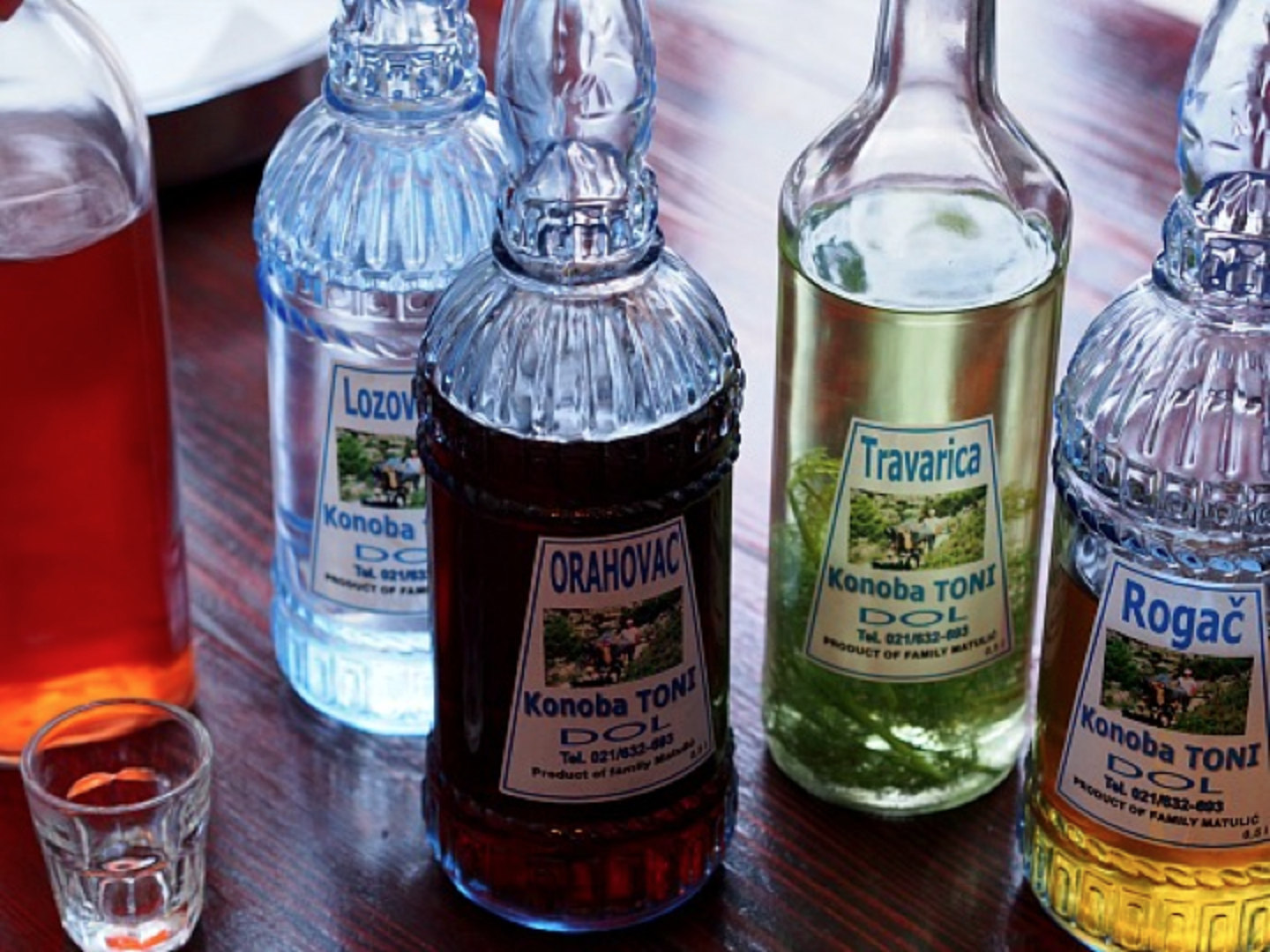 The image shows various bottles of alcoholic beverages, including a bottle of Drahova and Travanca, along with some glassware in the background.