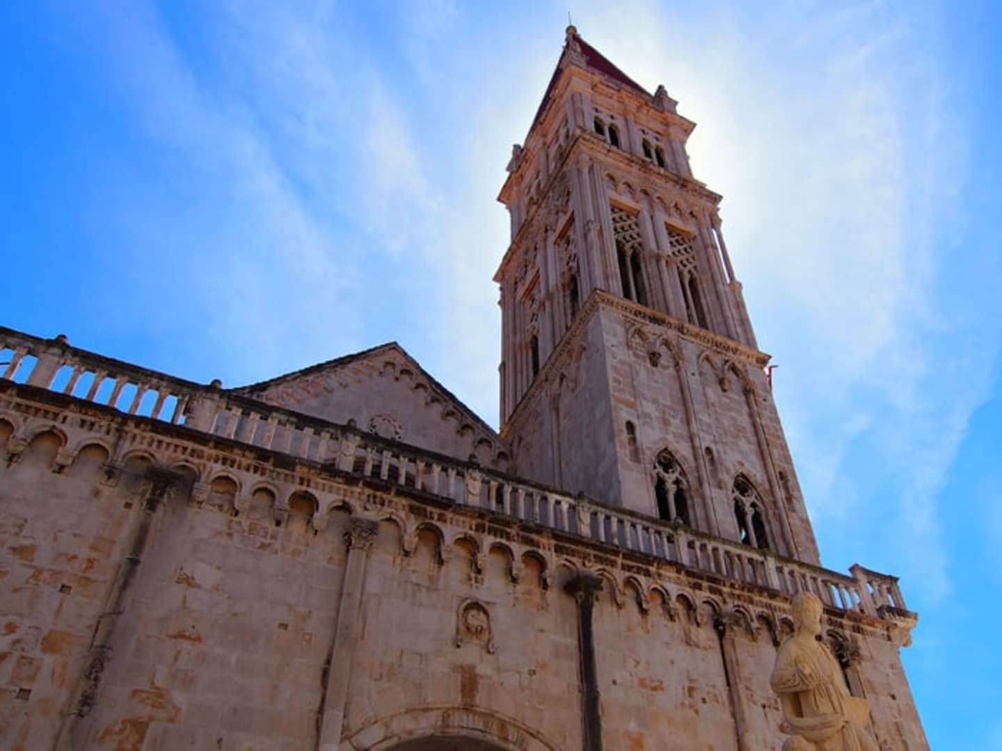 A towering stone cathedral with intricate architectural details stands against a bright blue sky, its ornate facade and bell tower commanding attention.