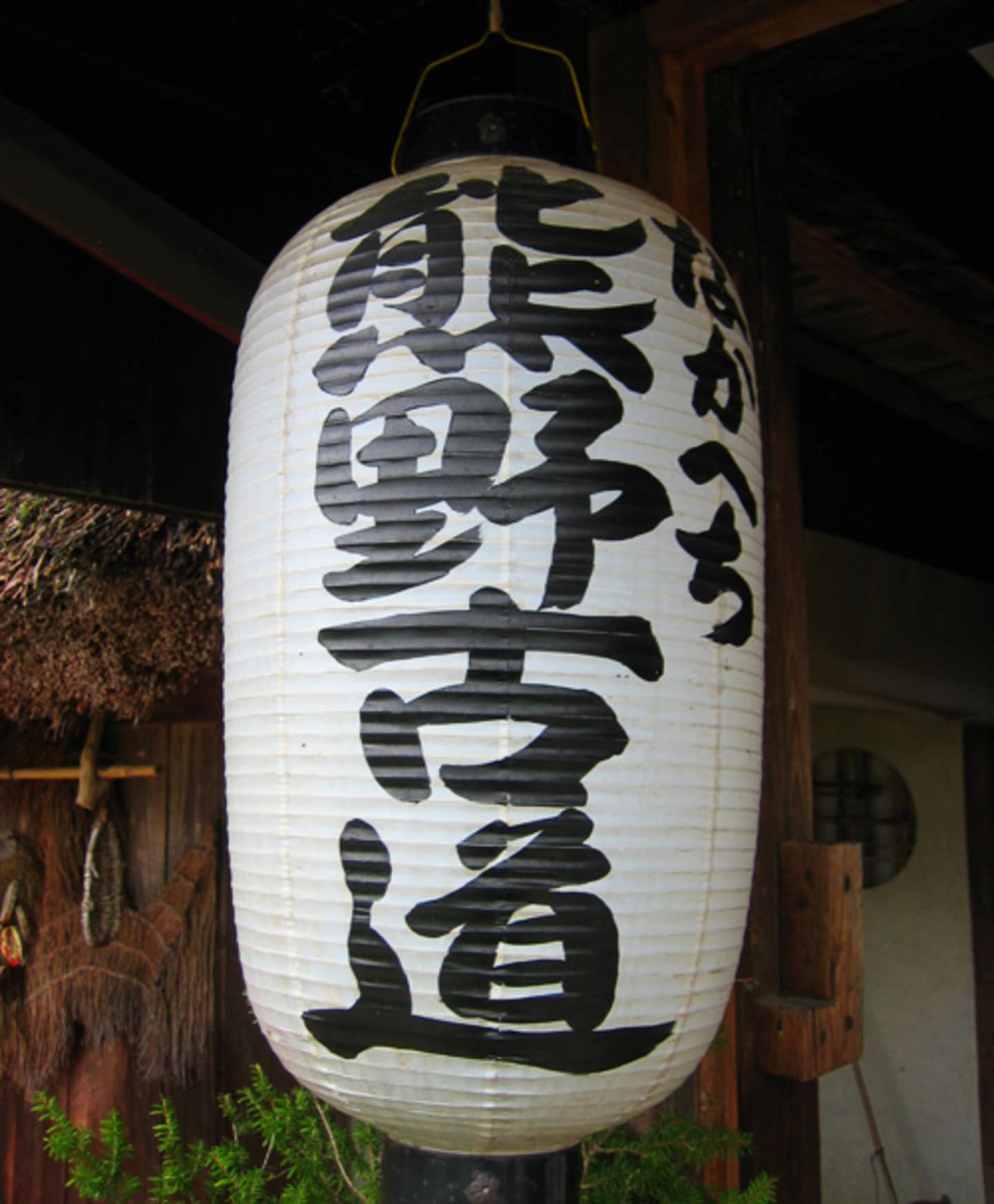 A white paper lantern with Japanese calligraphy hangs in a dimly lit, rustic-looking environment.