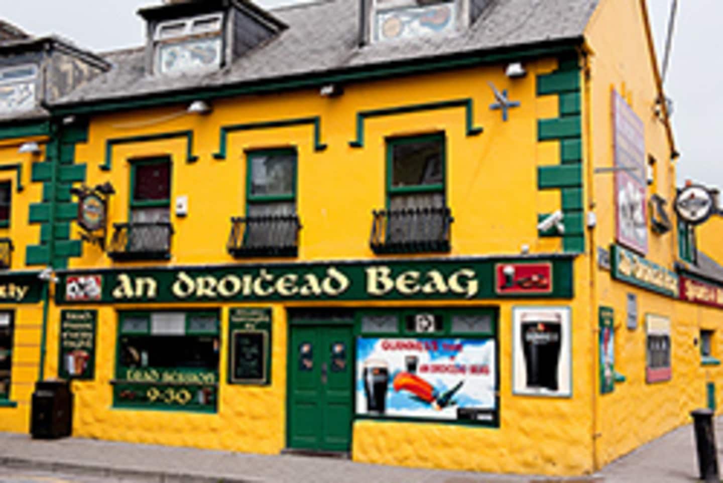 A vibrant, colorful building with a sign reading "An Droichead Beag" stands in the foreground, surrounded by other structures in the background.