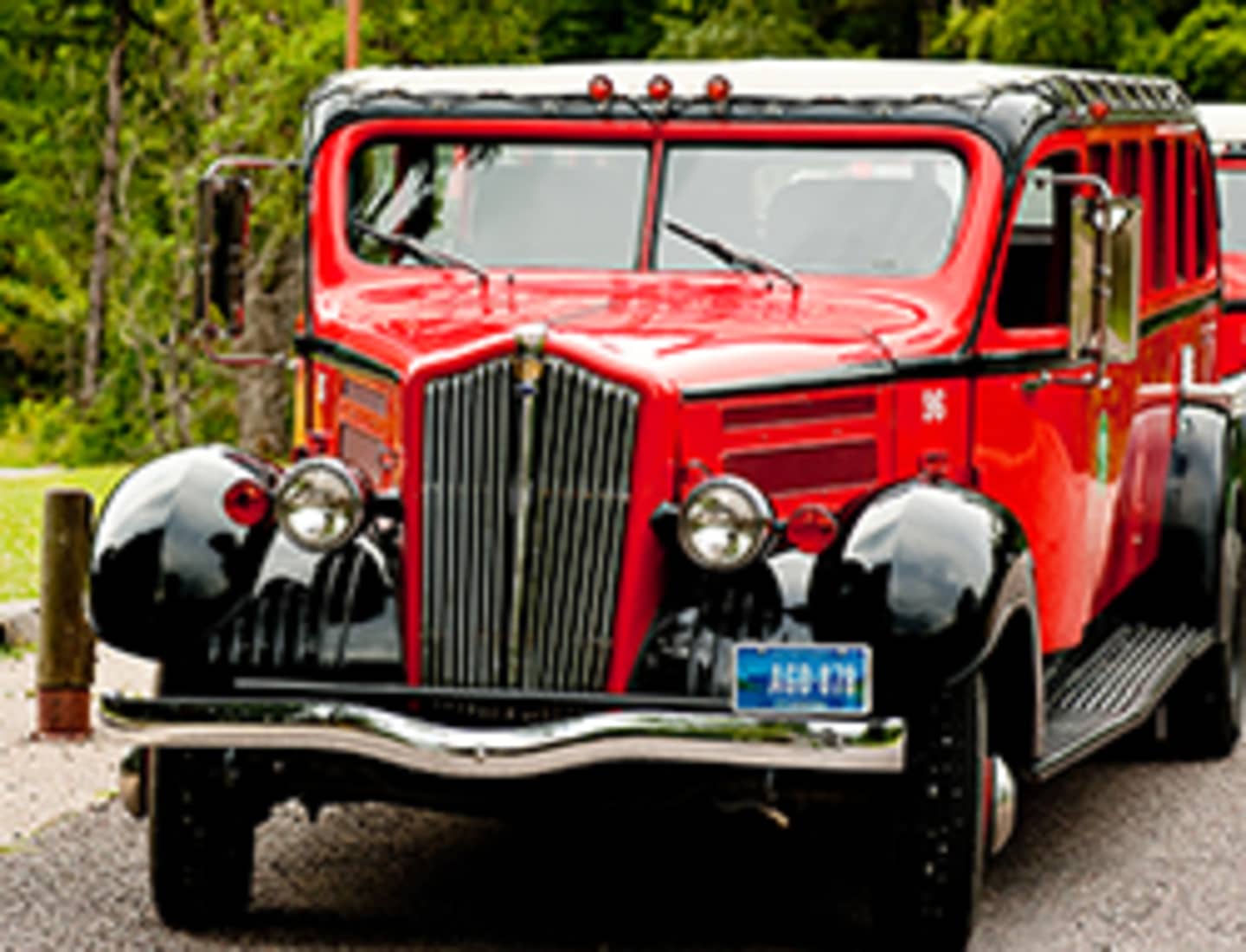 A vibrant red vintage truck stands prominently in the foreground, surrounded by lush greenery in the background.
